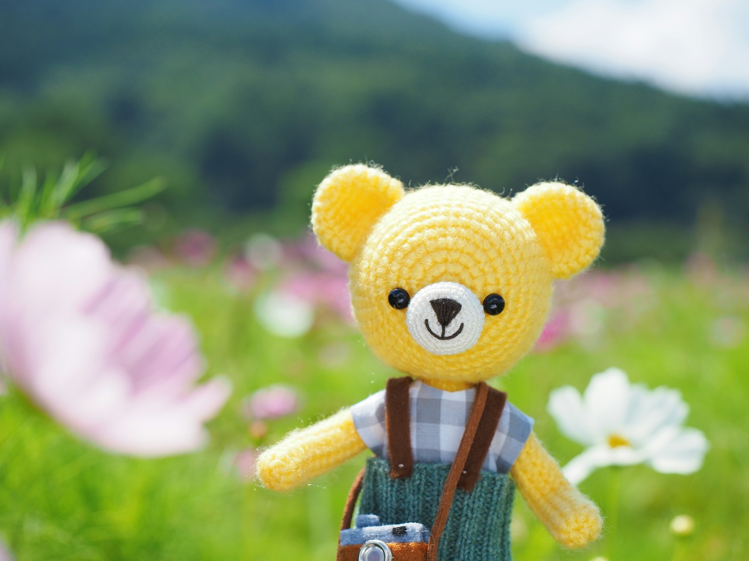 Un ours en peluche jaune au crochet se tenant dans un champ de fleurs