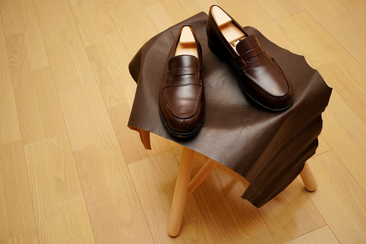 Brown leather shoes placed on a wooden stool with a leather sheet