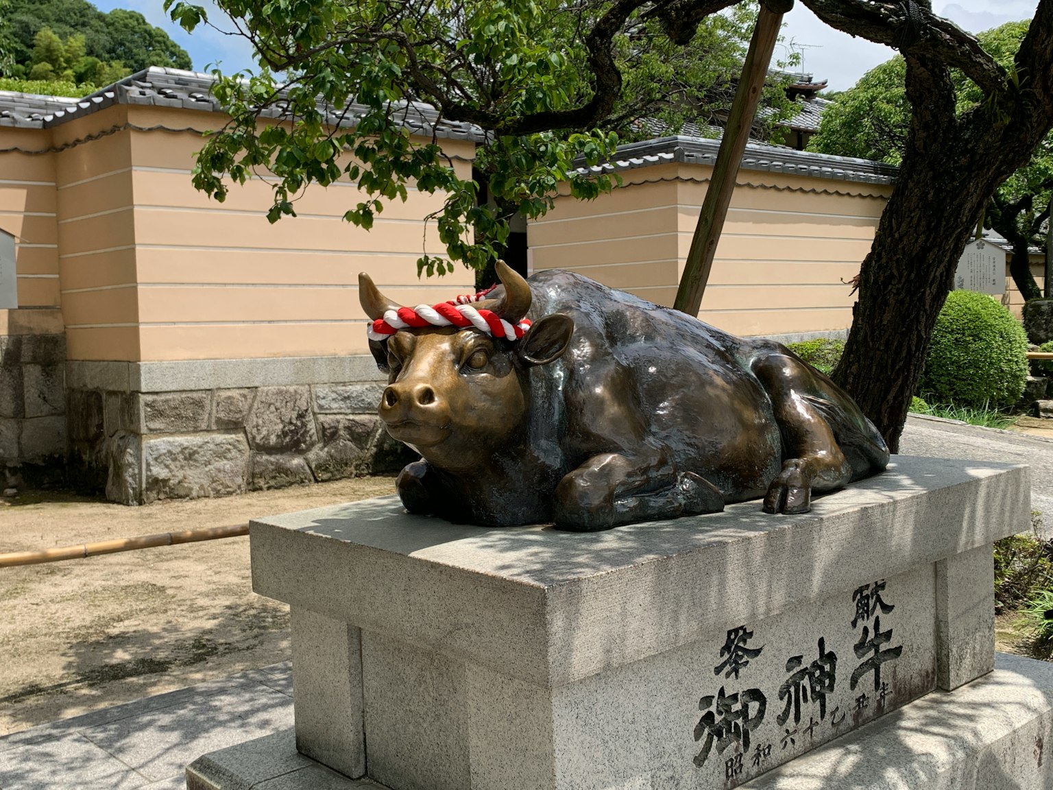 Una statua di bronzo di una mucca con una fascia decorativa su un piedistallo di pietra