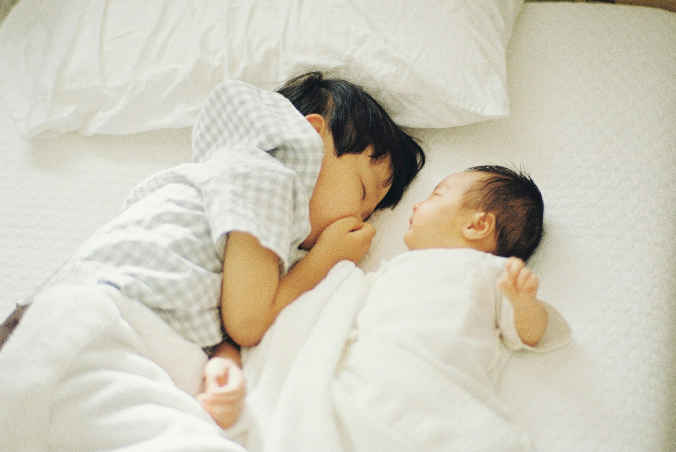 escena de dormitorio con un bebé y un niño durmiendo abrazados