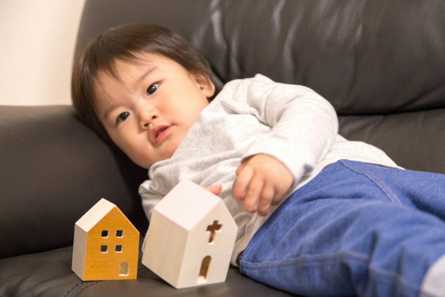 Young child lying on a sofa with wooden house toys