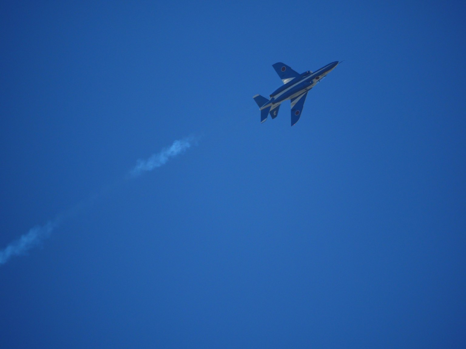 Un jet militar volando en un cielo azul con una estela de vapor blanca
