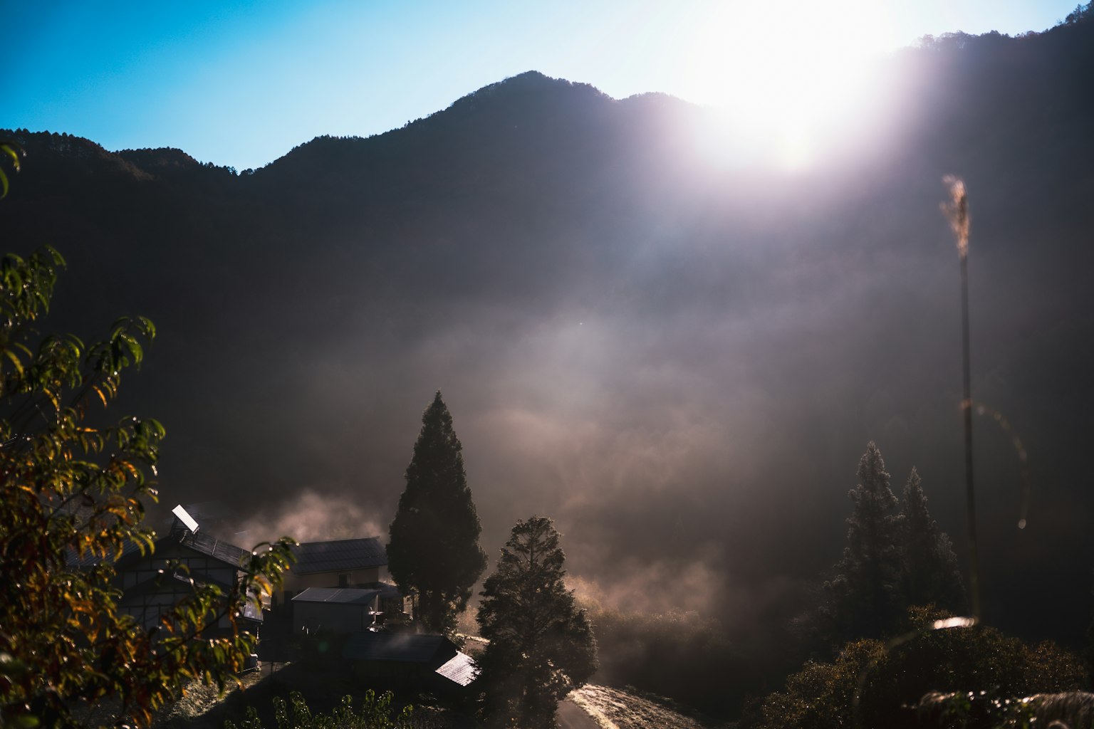 Pemandangan gunung saat matahari terbit dengan kabut yang menyelimuti pohon dan rumah