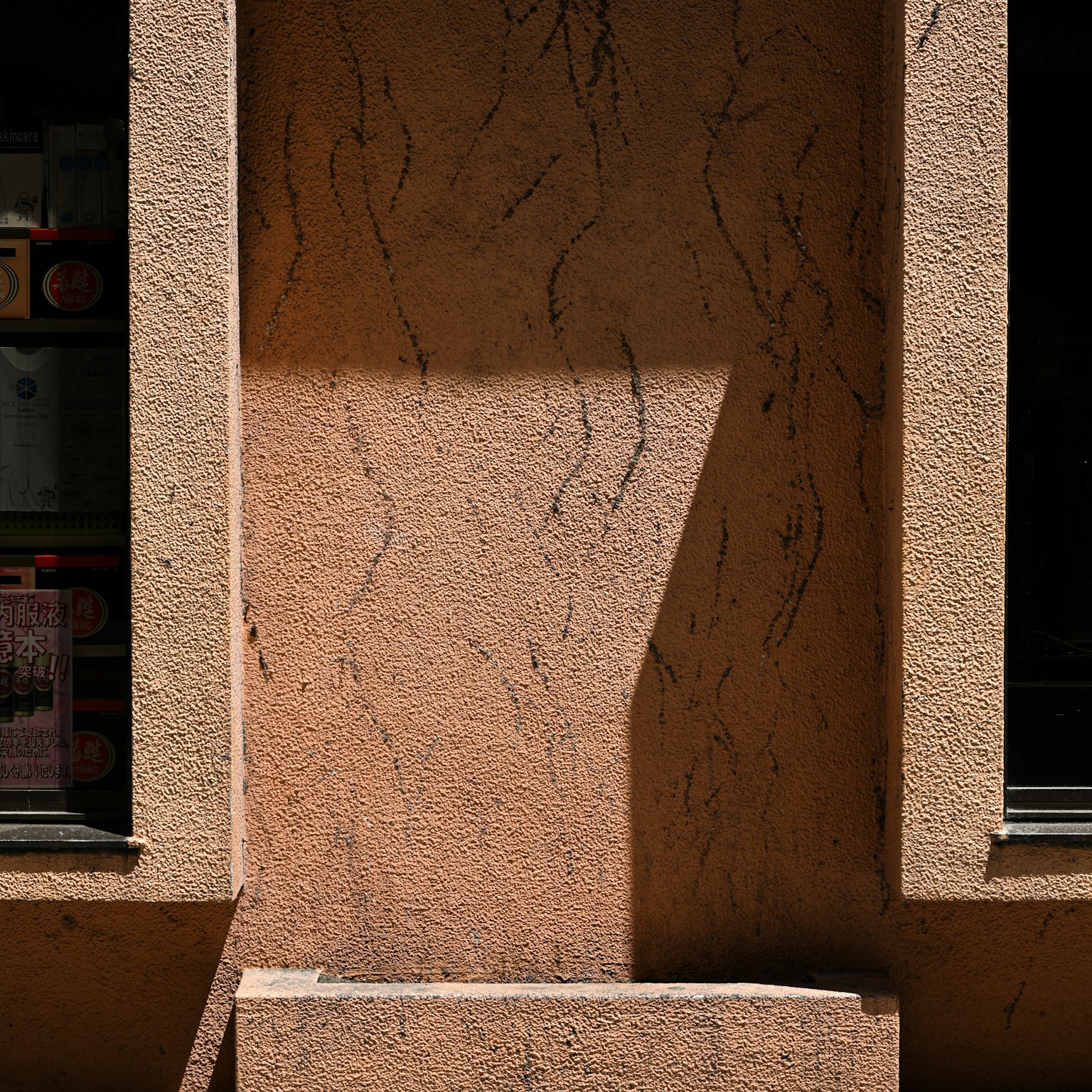 Sunlight casting a shadow on a light orange textured wall with a window