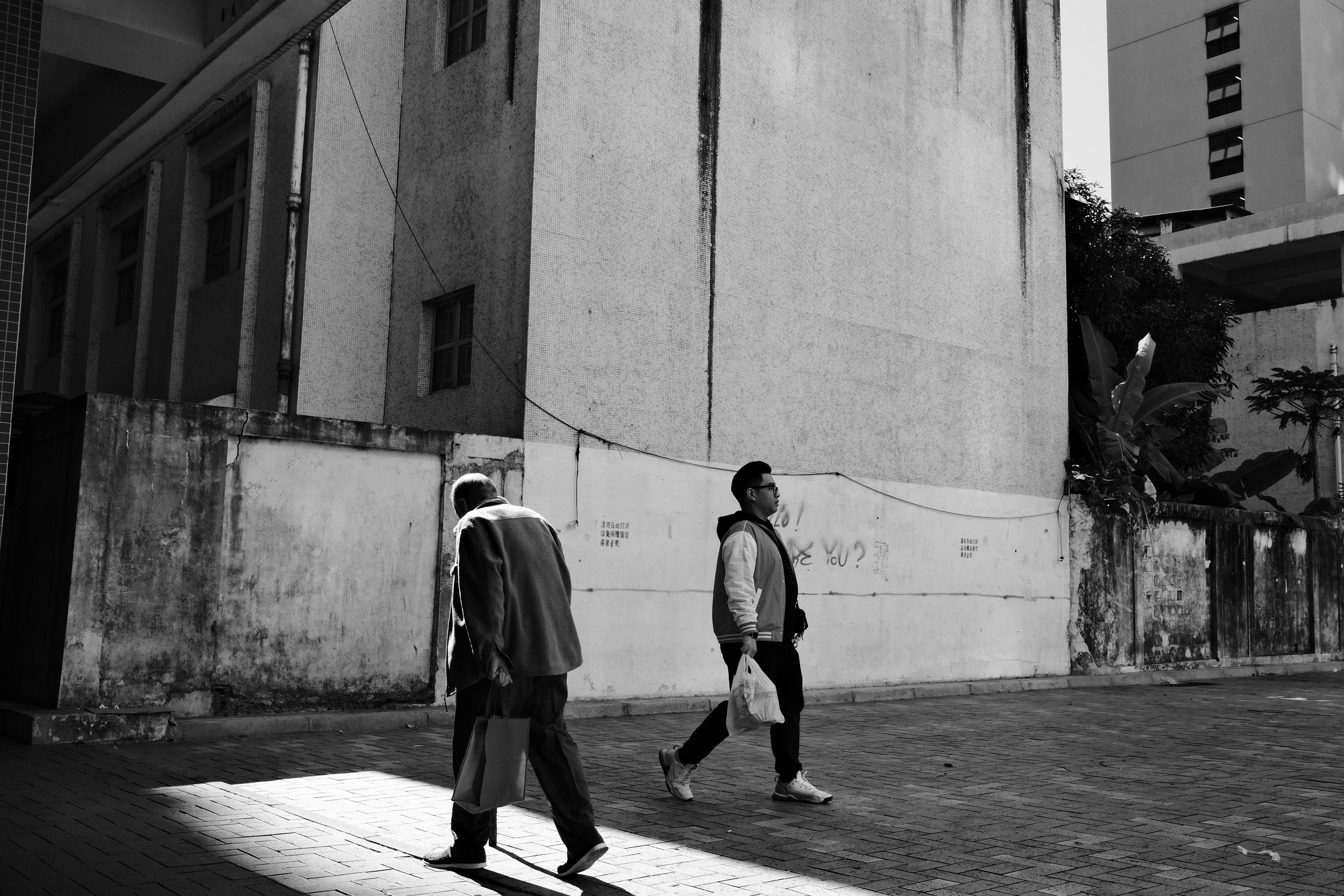 路地の壁沿いを歩く人々のモノクロ風景
