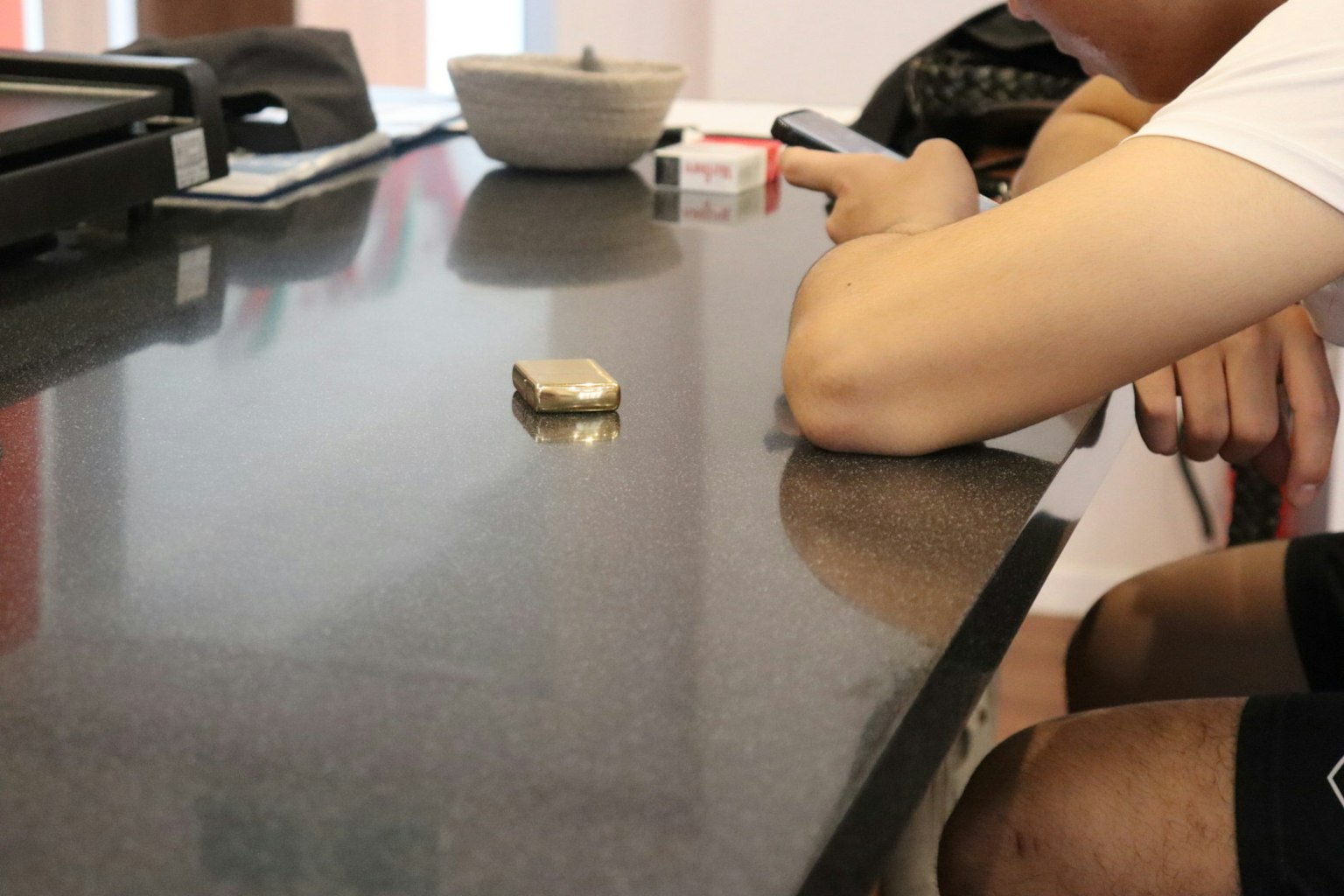 Un pequeño objeto en una mesa junto a una persona que sostiene un teléfono inteligente