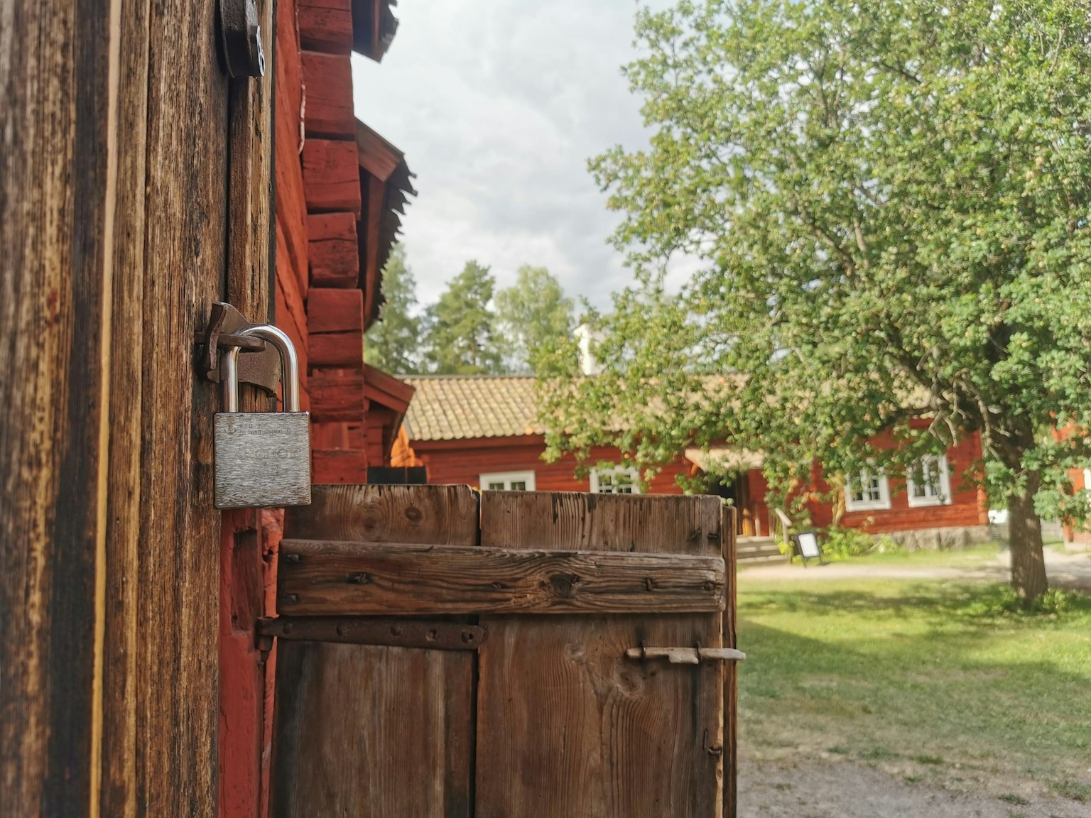 Rustic scene featuring a wooden door with a padlock and red buildings in the background