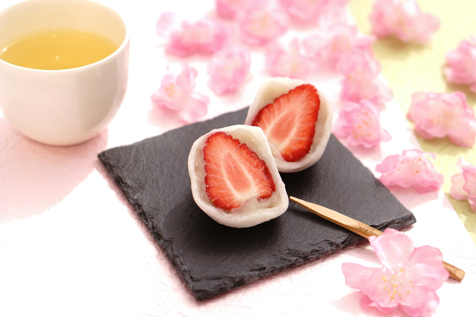 Daifuku stroberi yang disusun dengan indah di atas batu hitam dengan teh hijau dan bunga sakura