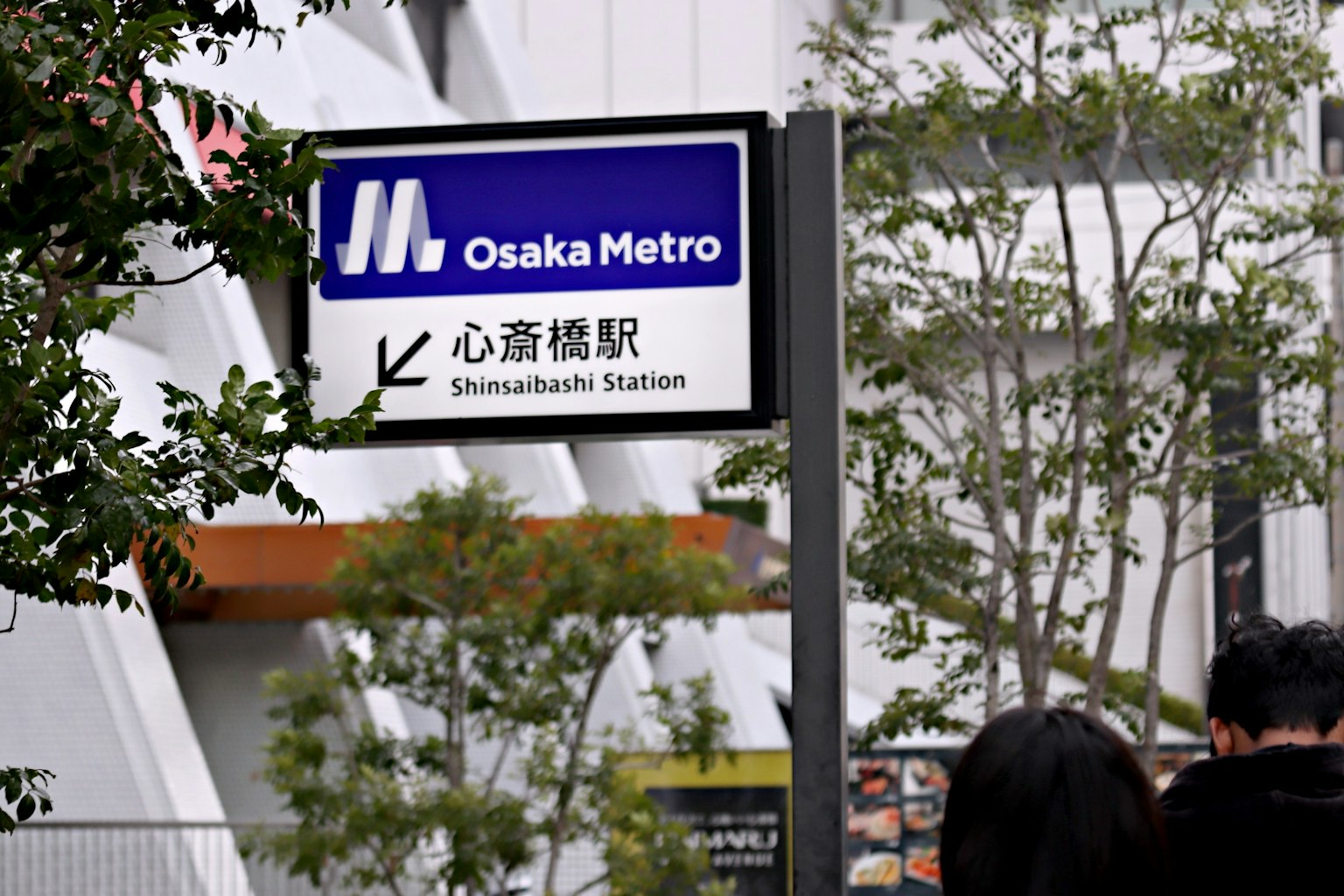 Schild der U-Bahn-Station Shinsaibashi in Osaka mit umliegendem Grün