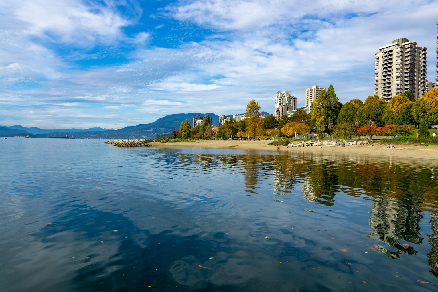 Pemandangan pantai yang indah di Vancouver mencerminkan langit biru dan awan di atas air pepohonan berwarna dan gedung pencakar langit