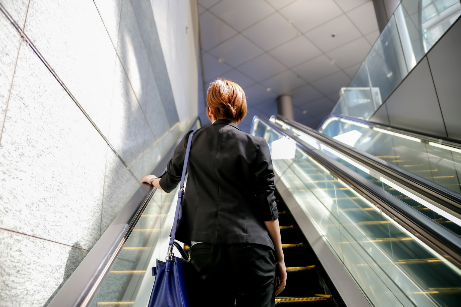 Mujer en traje de negocios subiendo una escalera mecánica