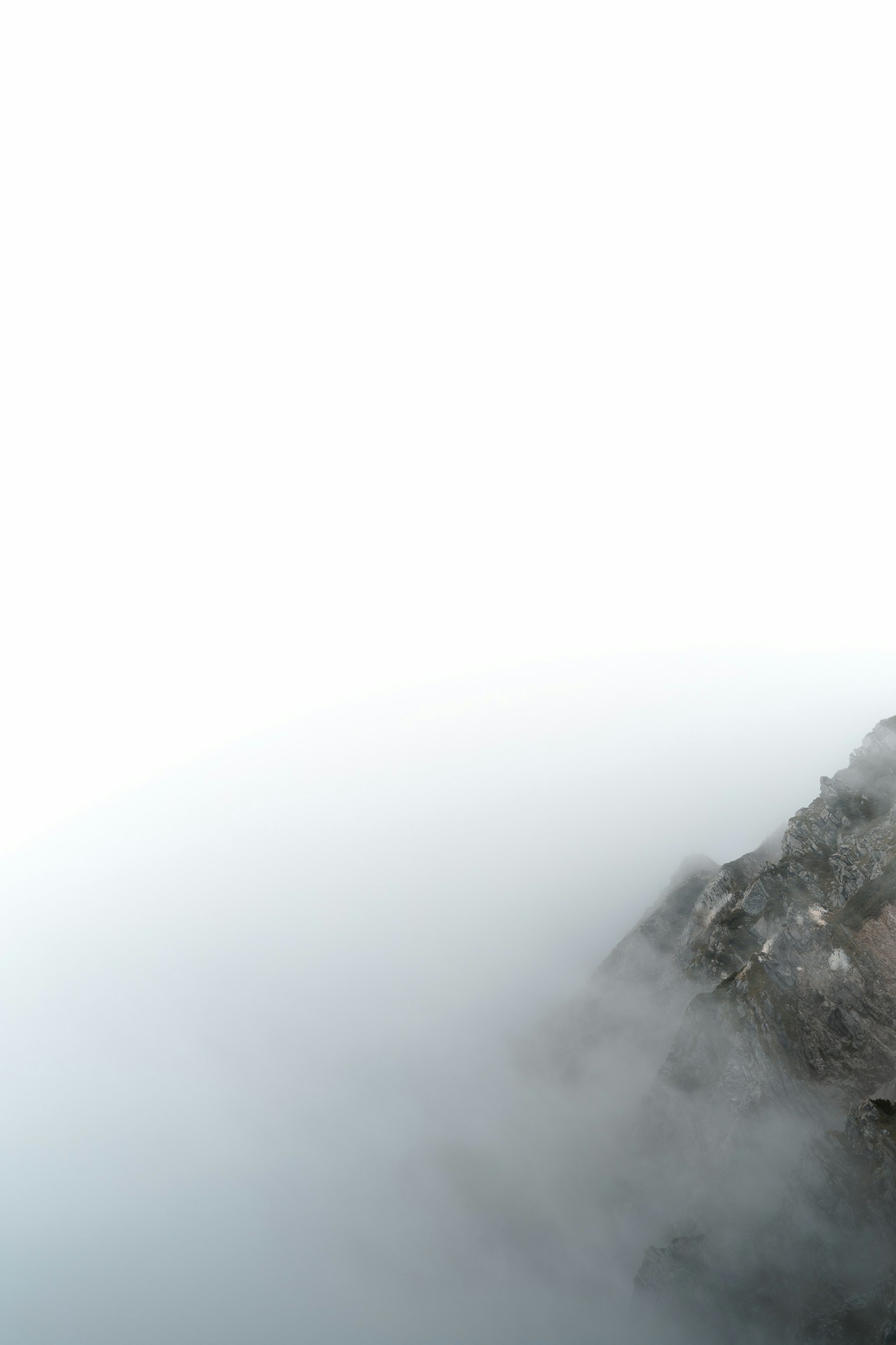 Part of a rocky cliff shrouded in fog with bright sky