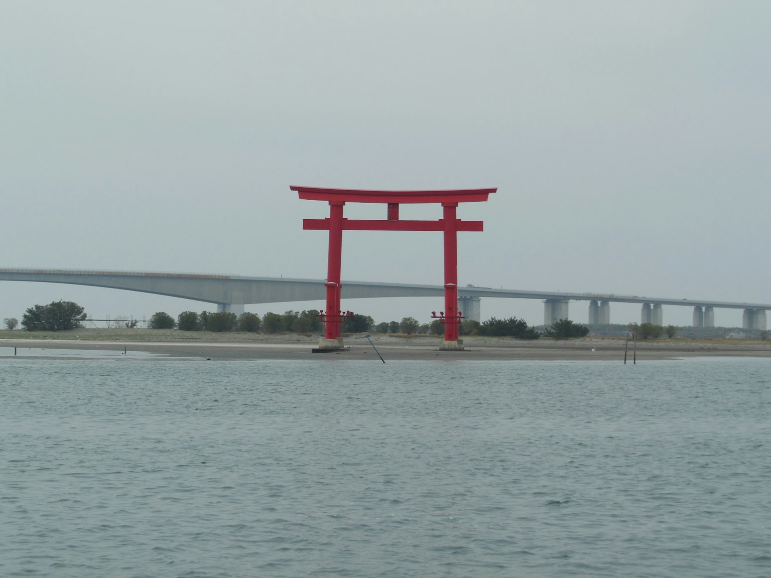 红色鸟居矗立在水中，背景有一座桥