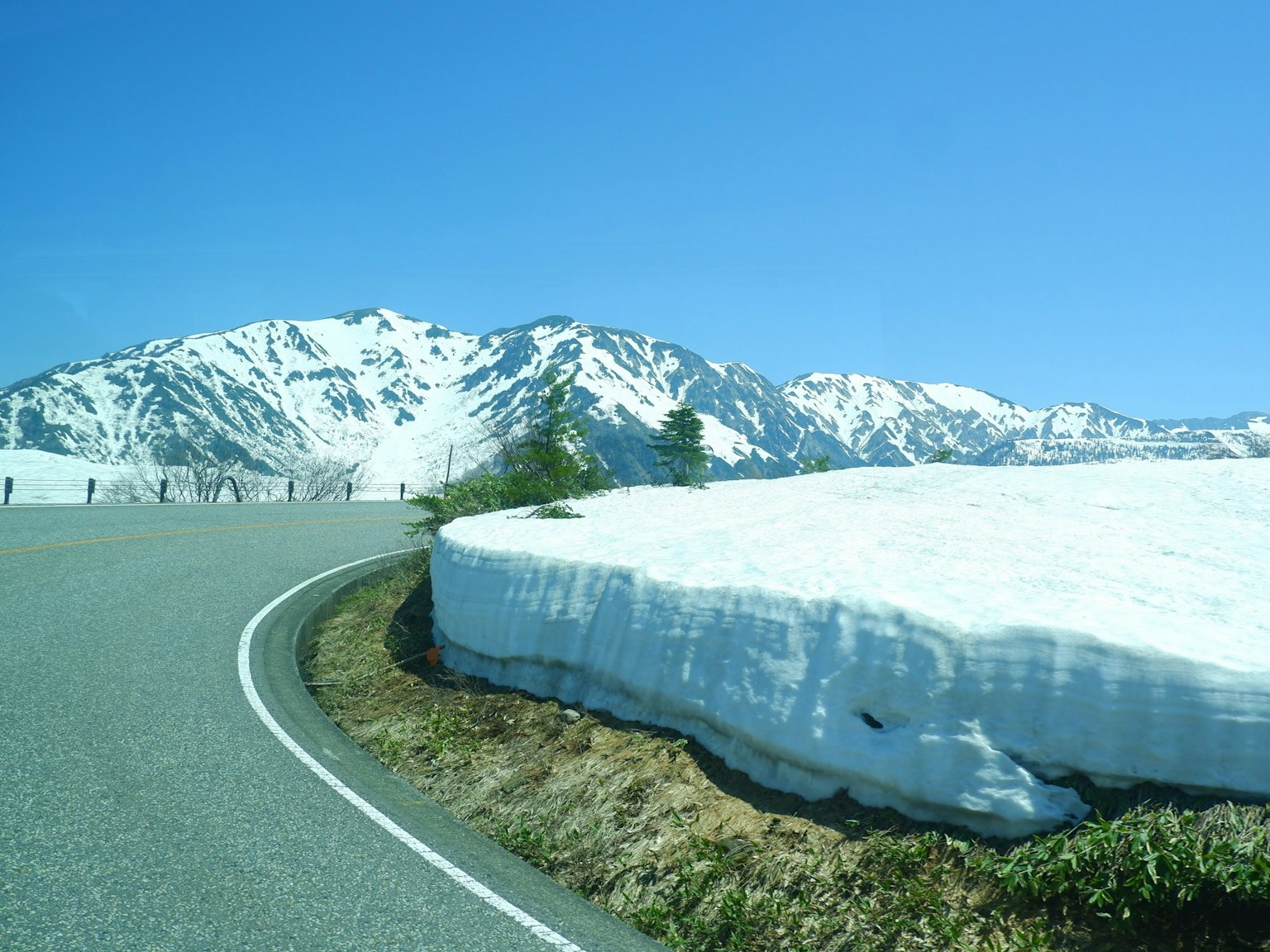 Carretera curva junto a montañas nevadas bajo un cielo azul claro