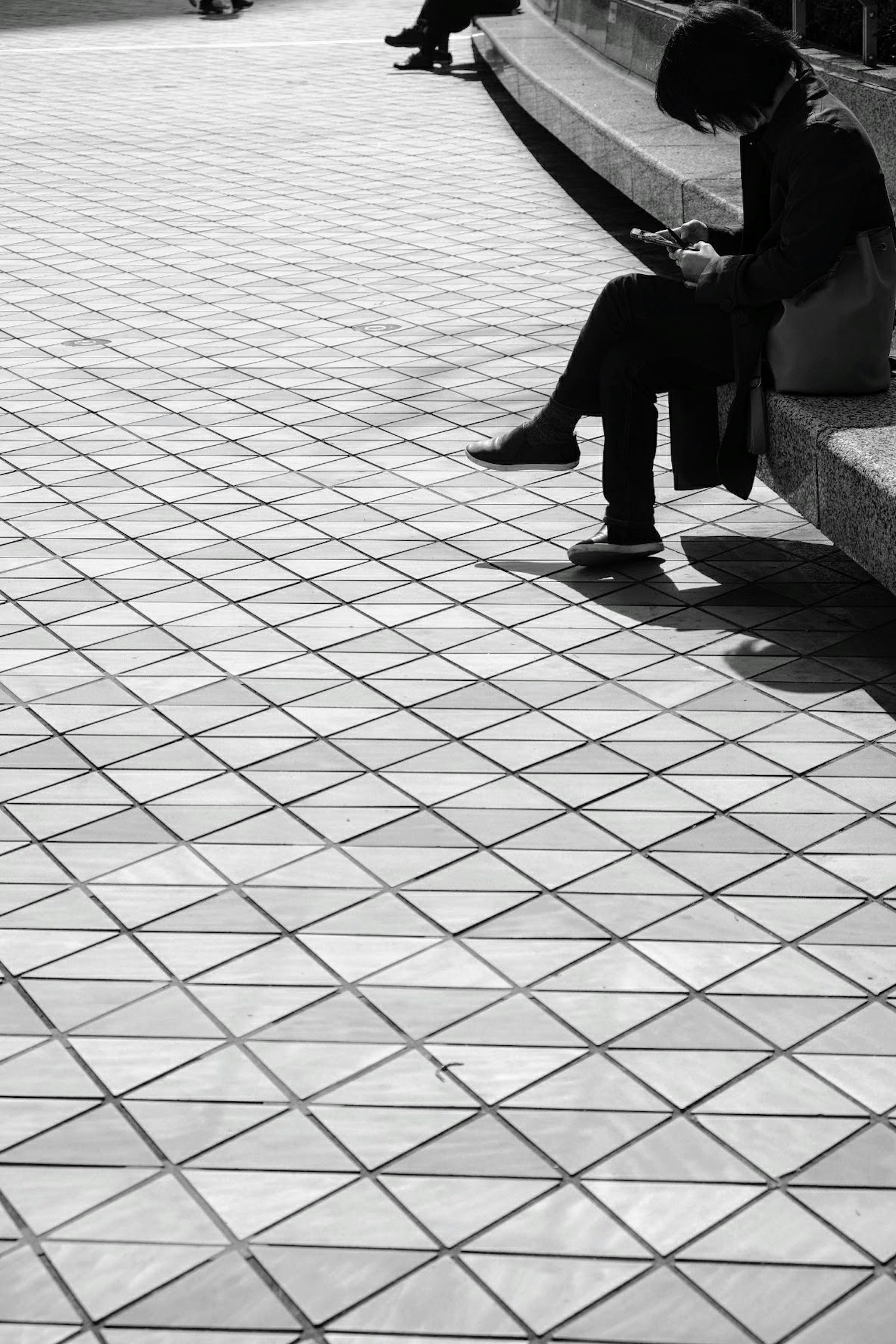 A person sitting and looking at a smartphone in a black and white urban setting