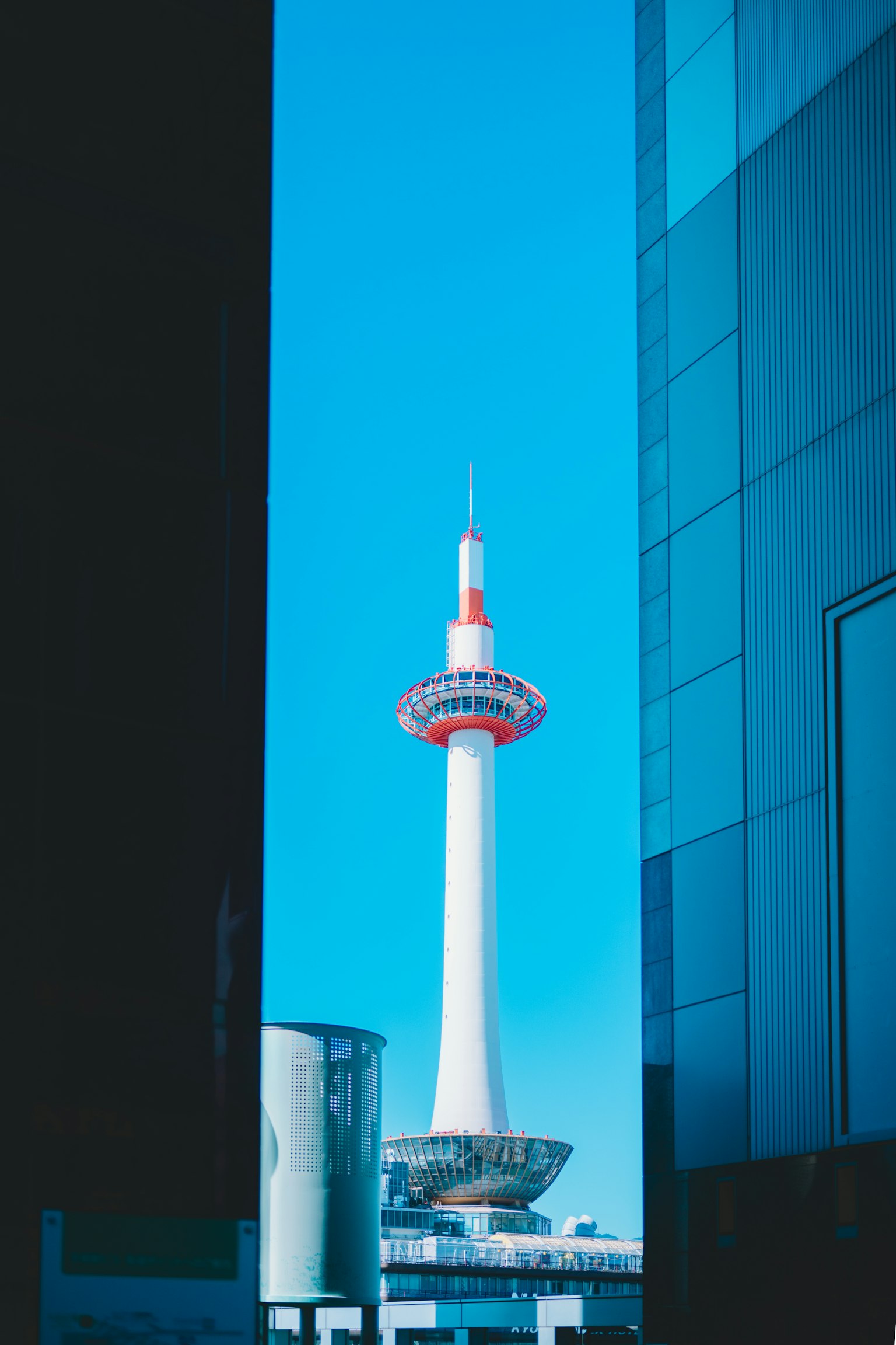 Vista de la Torre de Kioto enmarcada entre edificios modernos bajo un cielo azul claro
