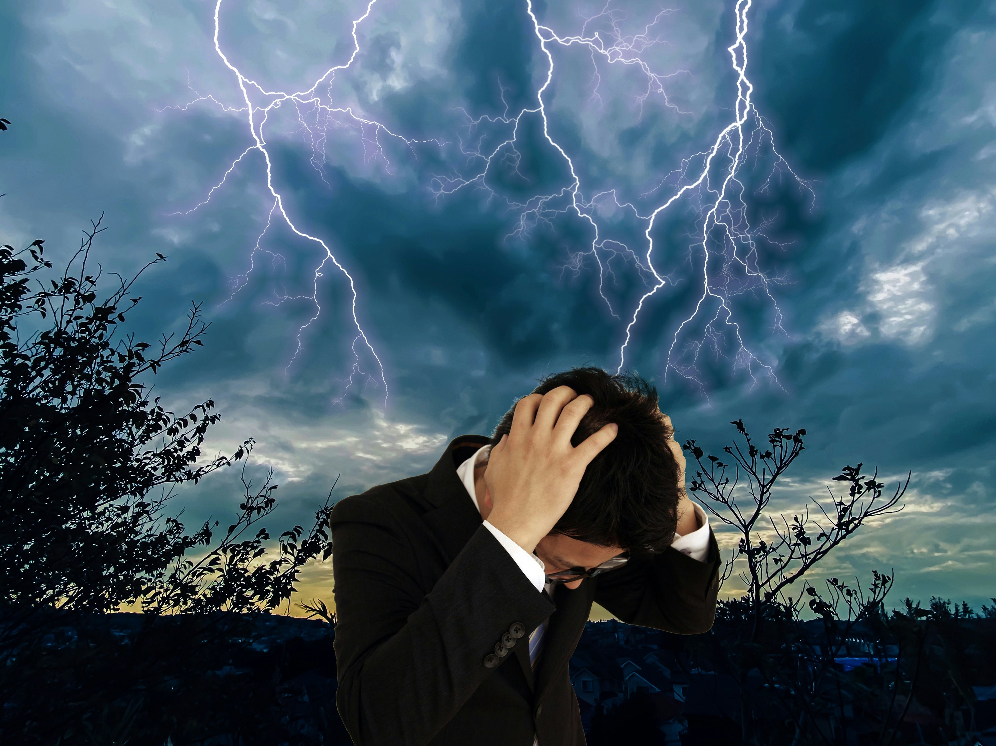 雷雲の下で頭を抱えるスーツ姿の男性
