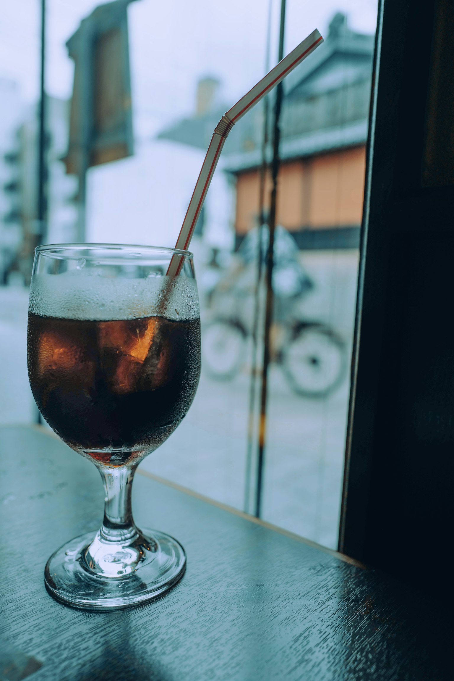 Một ly cola với ống hút trên bàn cạnh cửa sổ