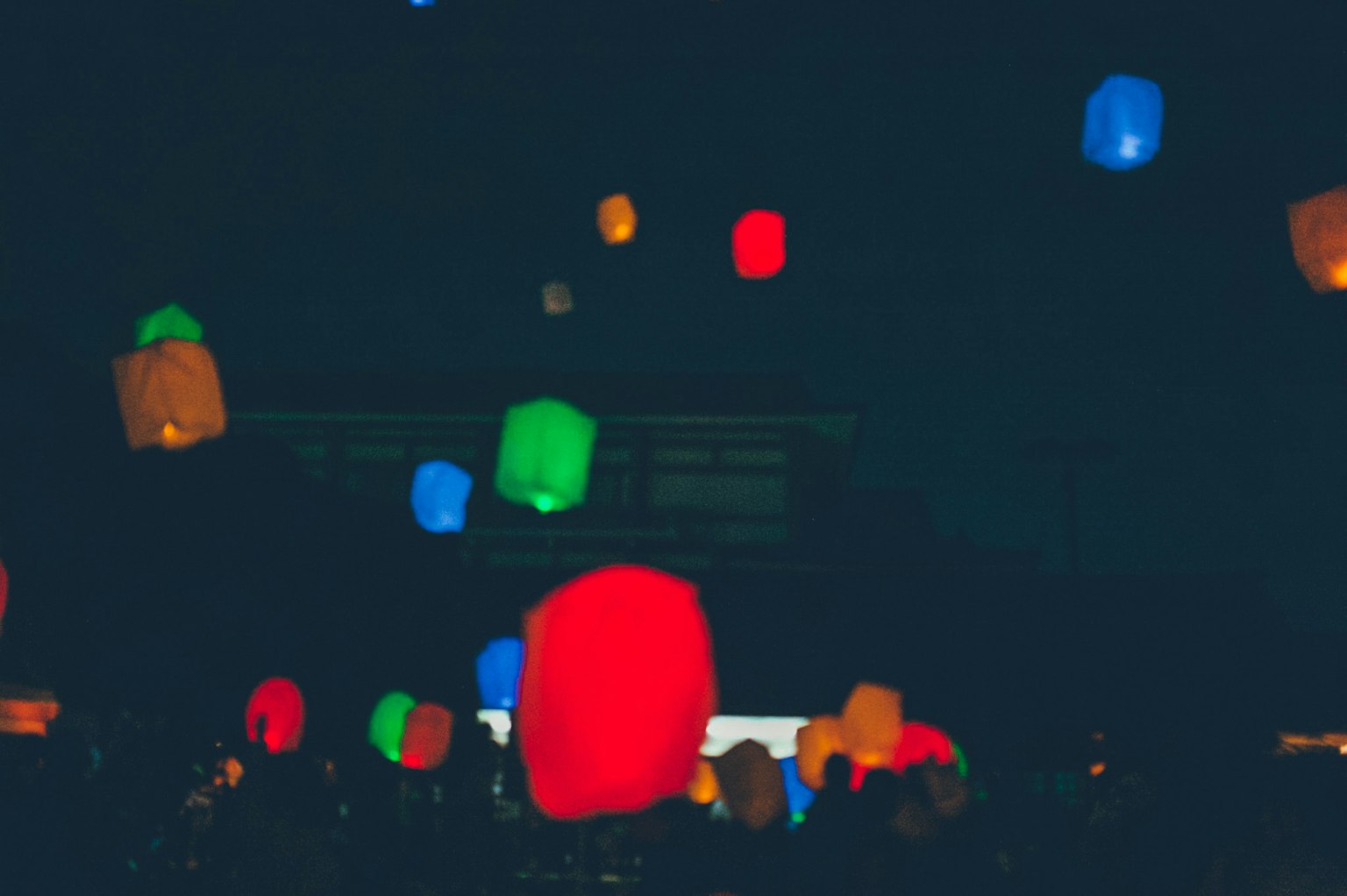 Des lanternes colorées flottant dans le ciel nocturne sur un fond sombre