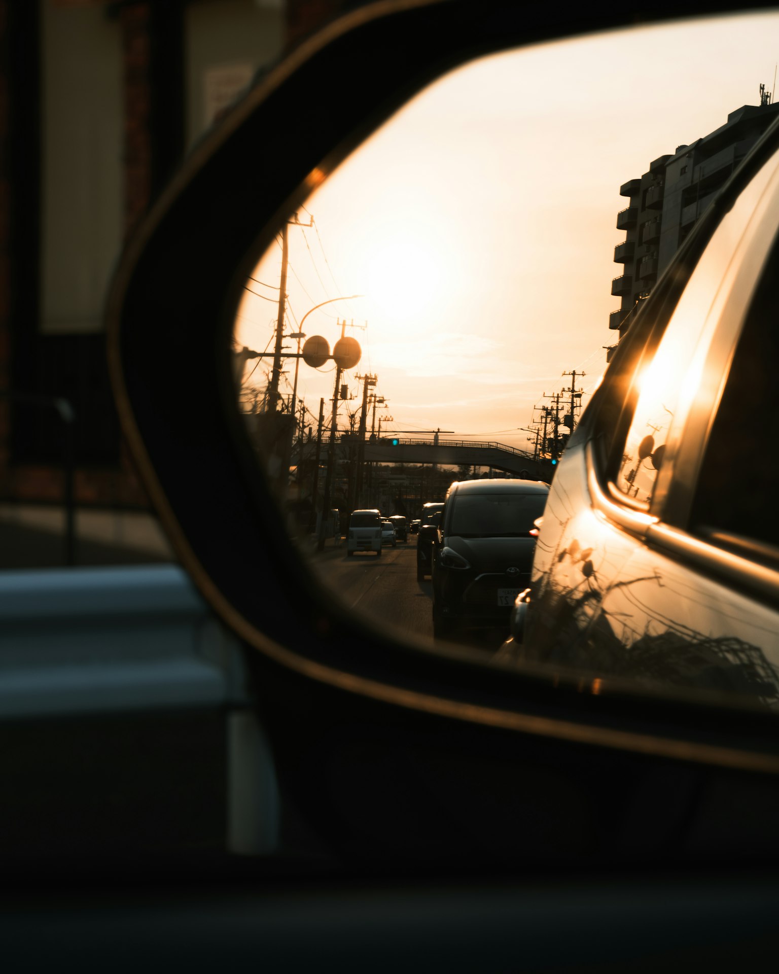A side mirror reflecting the sunset and traffic in the background
