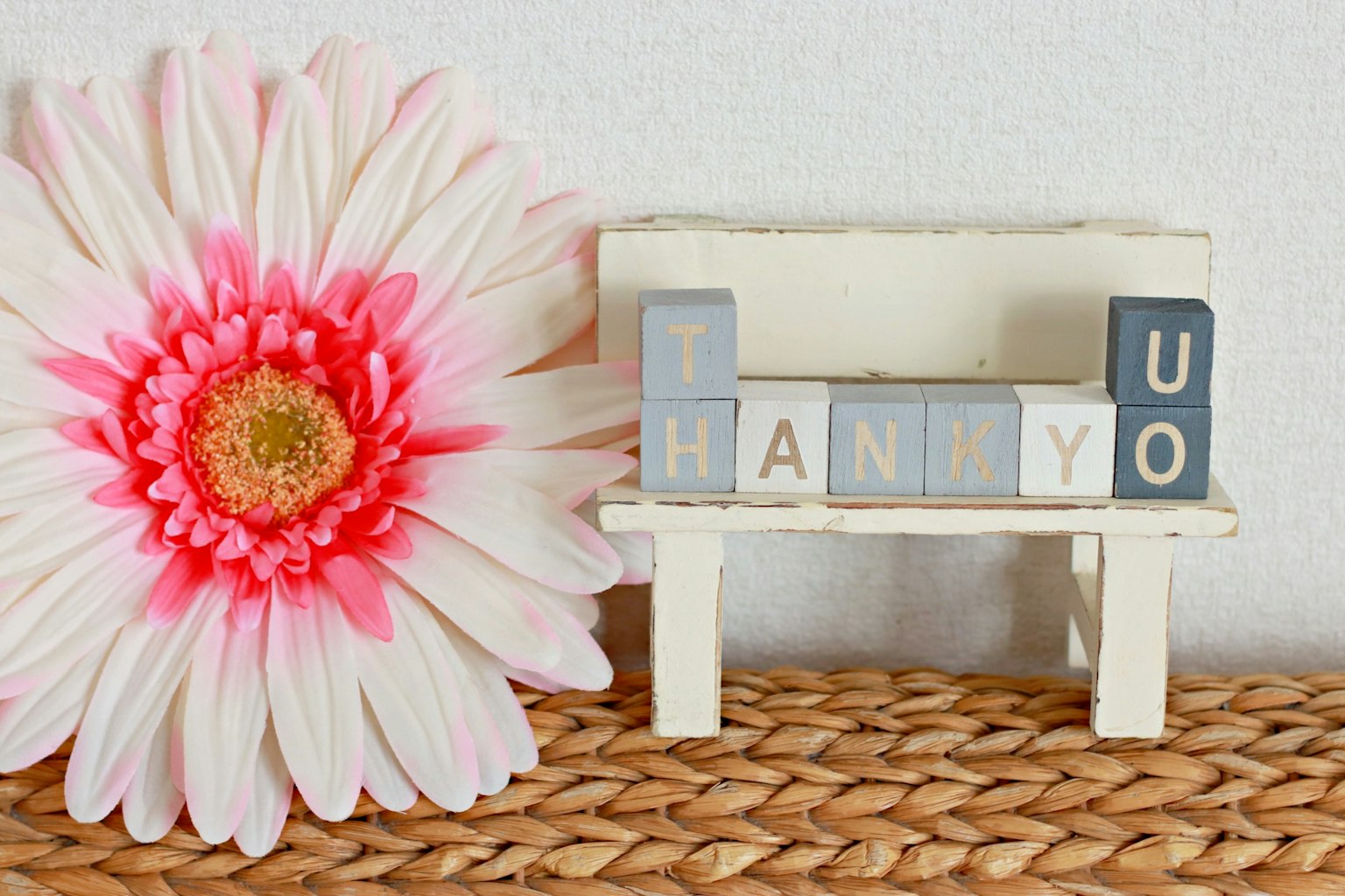 Un pequeño banco blanco con bloques de letras que dicen gracias junto a una gran flor rosa
