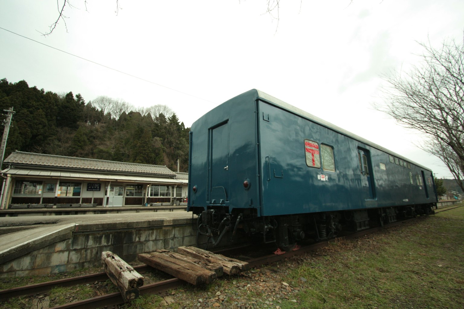 Wagon de train bleu garé sur une zone herbeuse près d'une gare