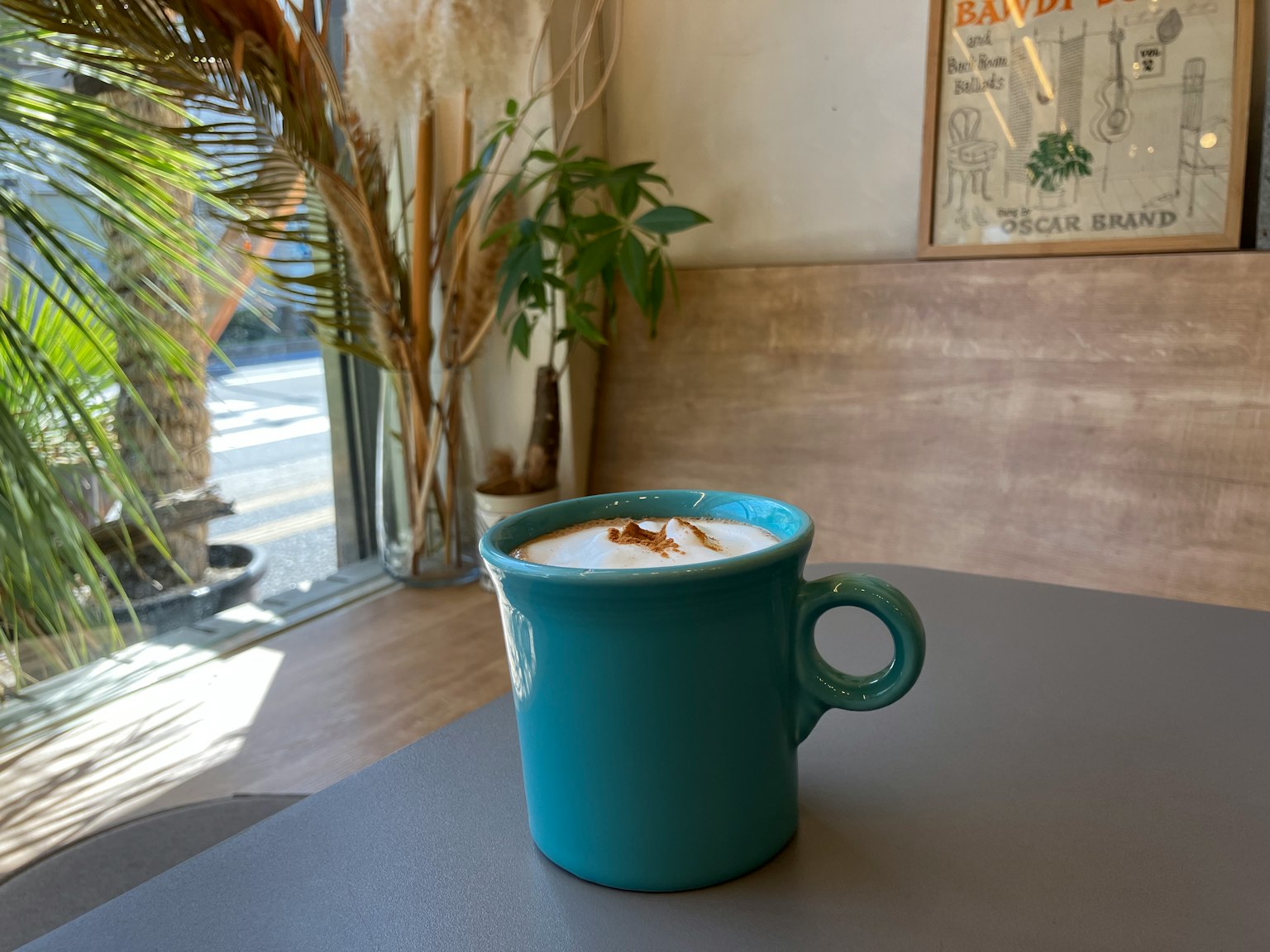 A teal coffee cup on a table in a cafe with plants and natural light