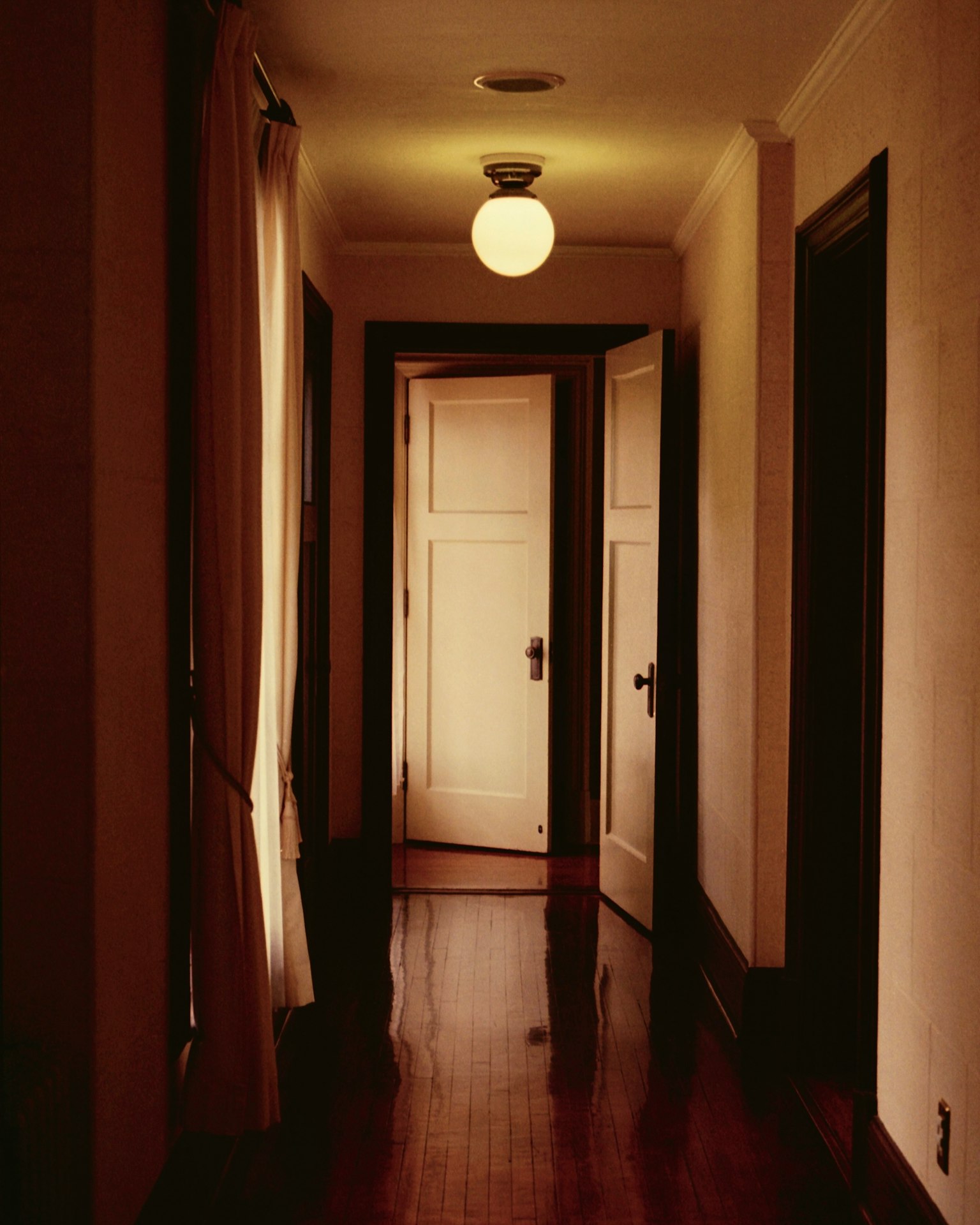 Corridoio con illuminazione brillante e pavimento in legno con porte