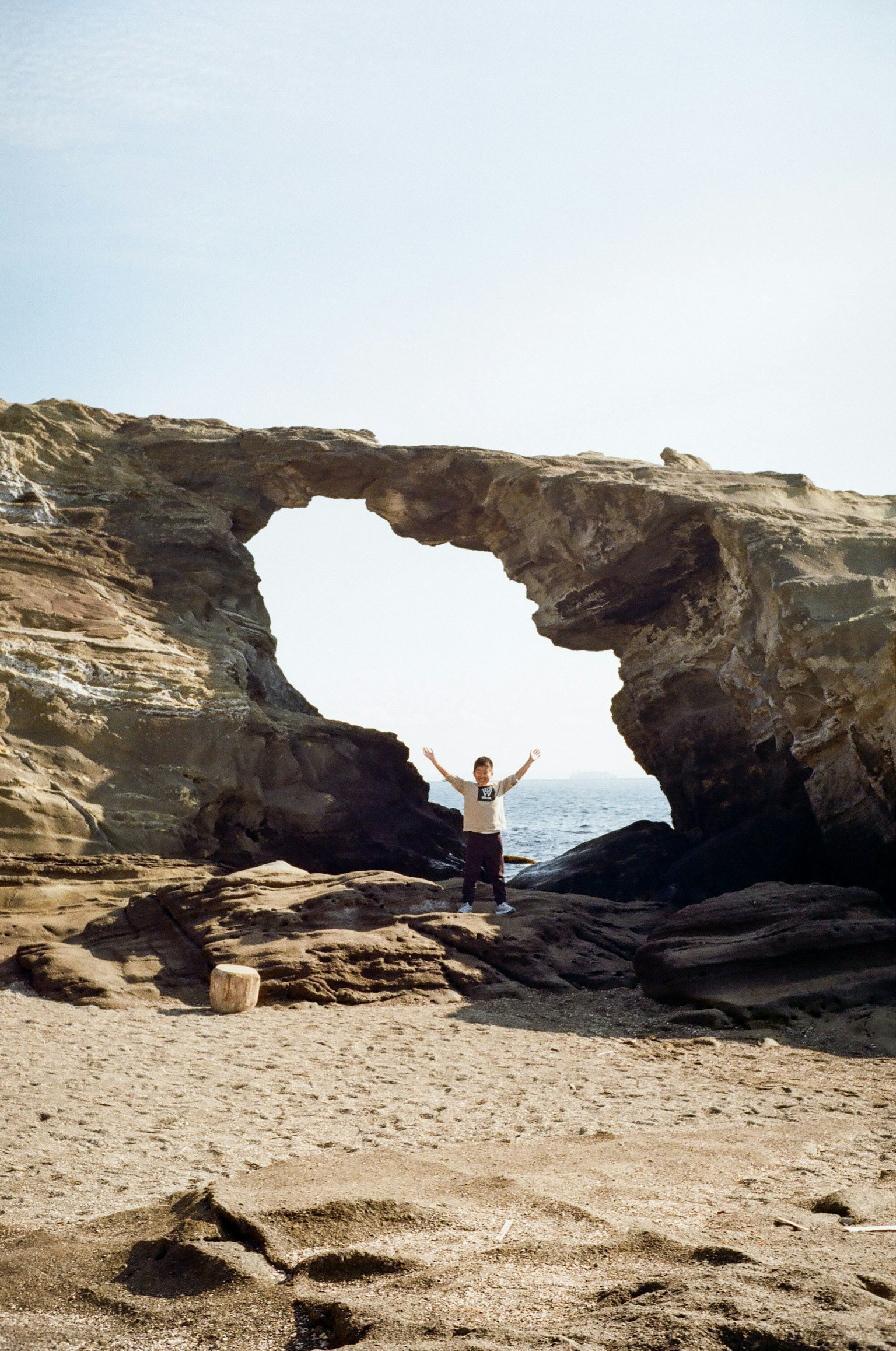 Persona in piedi davanti a un grande arco di roccia vicino al mare