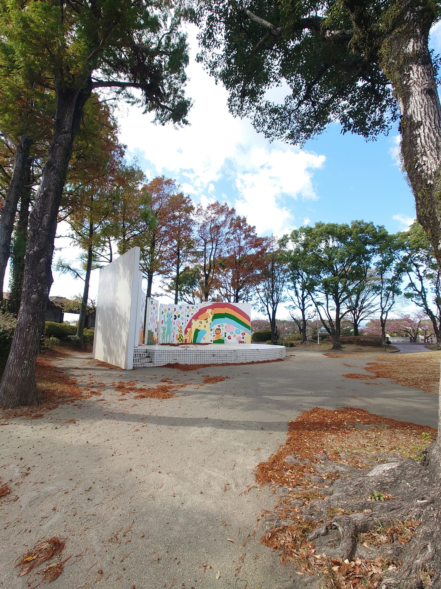 Eine Parkszene mit einem bunten Regenbogenmural umgeben von Bäumen und gefallenen Blättern