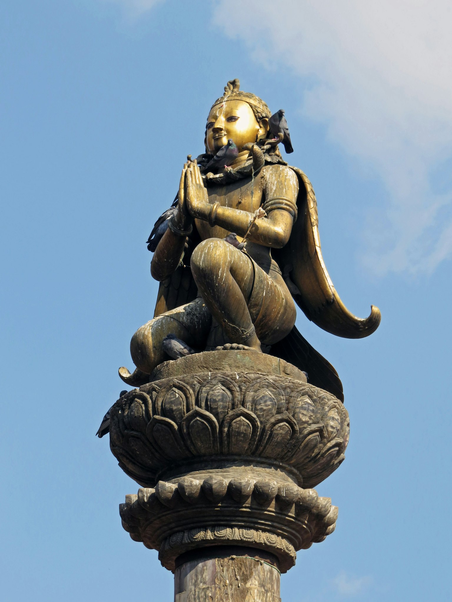 Statua di una divinità in posizione di preghiera con caratteristiche dorate contro un cielo blu