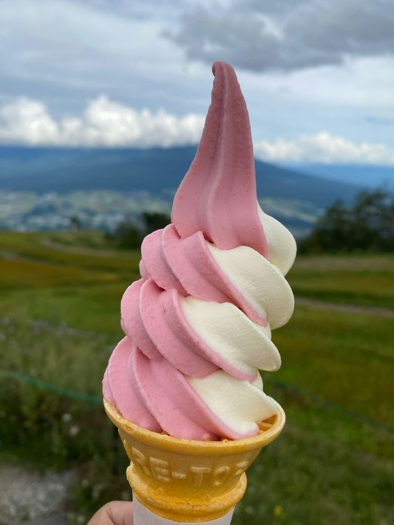Un helado suave rosa y blanco en un cono con un fondo montañoso pintoresco