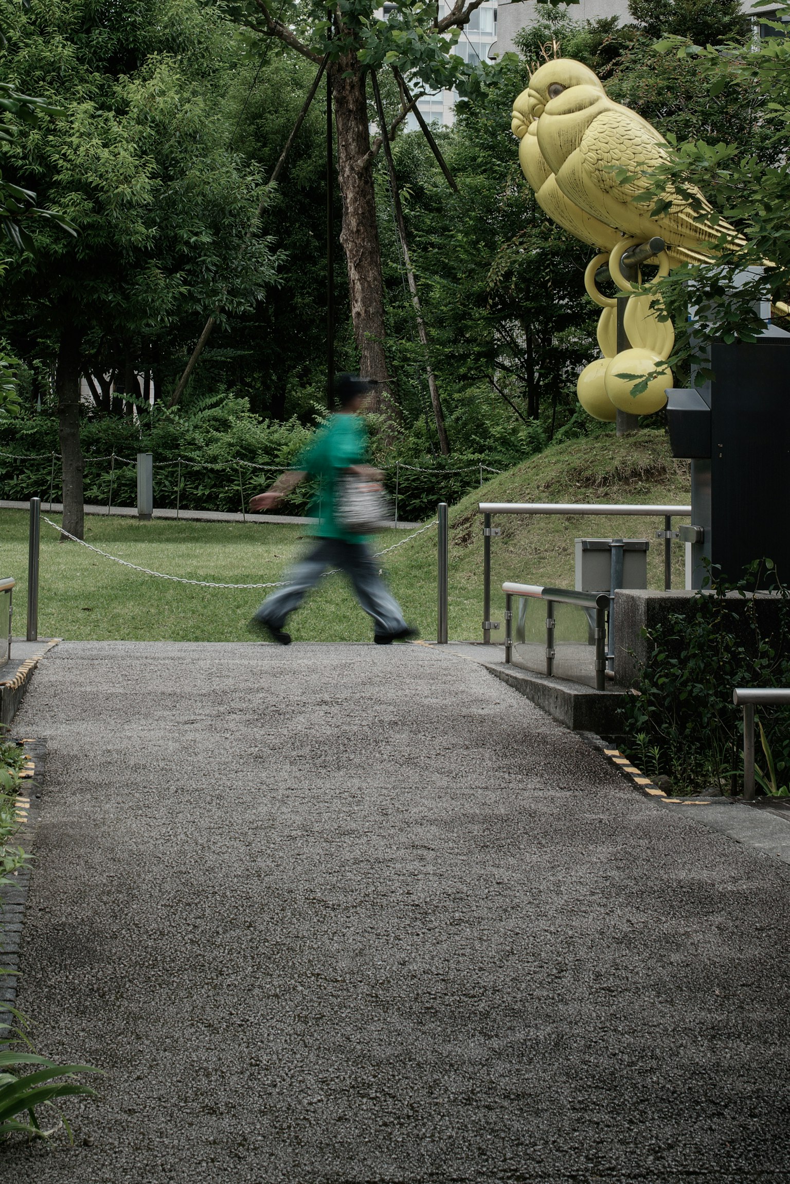 Una persona caminando por un sendero del parque con una gran escultura de ave amarilla