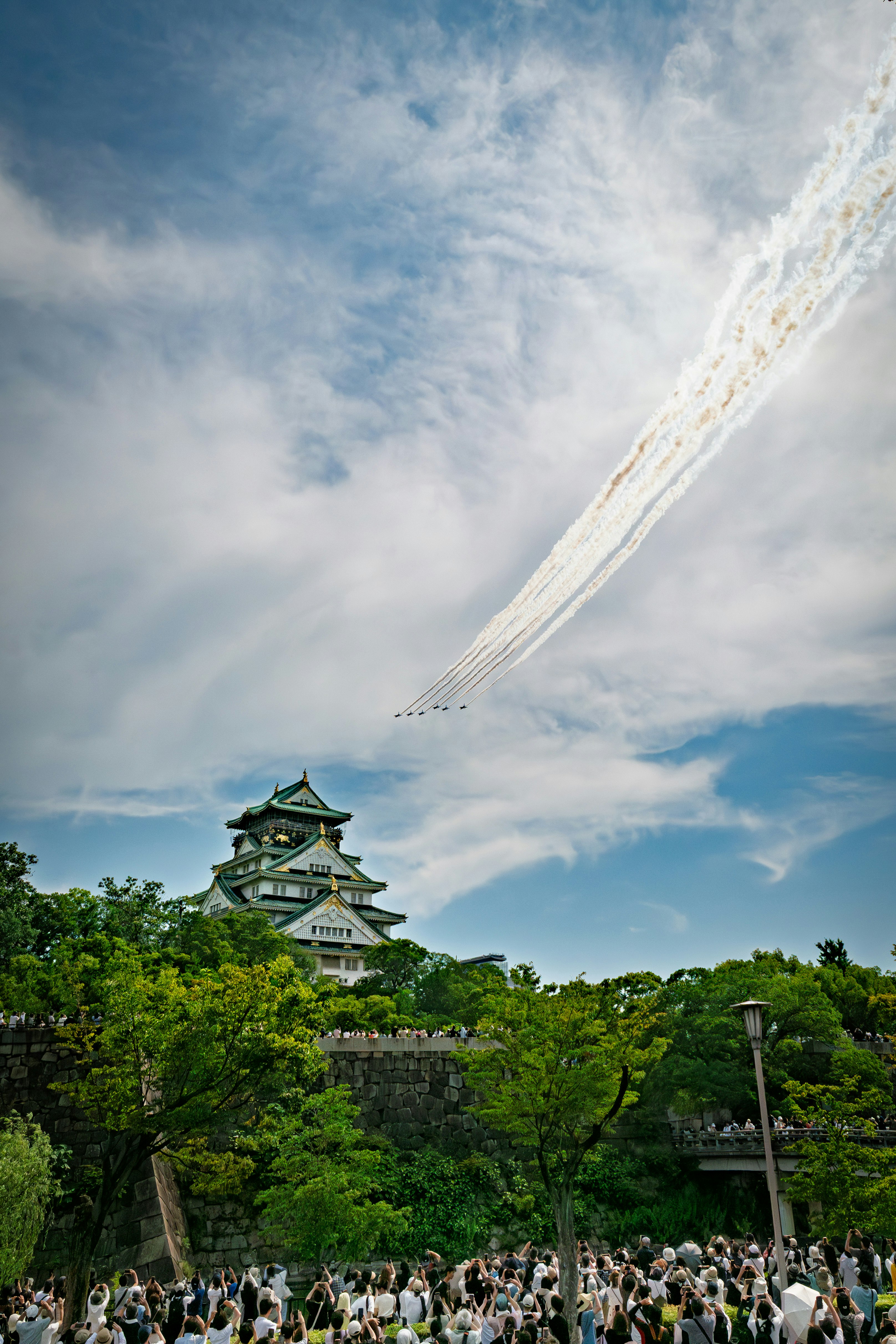 castle surrounded by trees with a crowd under a blue sky