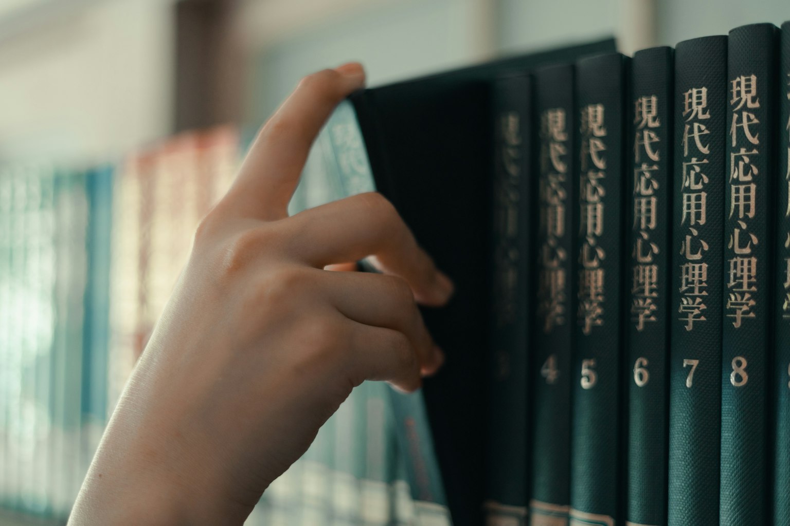 Una mano alcanzando un libro en una estantería con títulos de psicología aplicada moderna