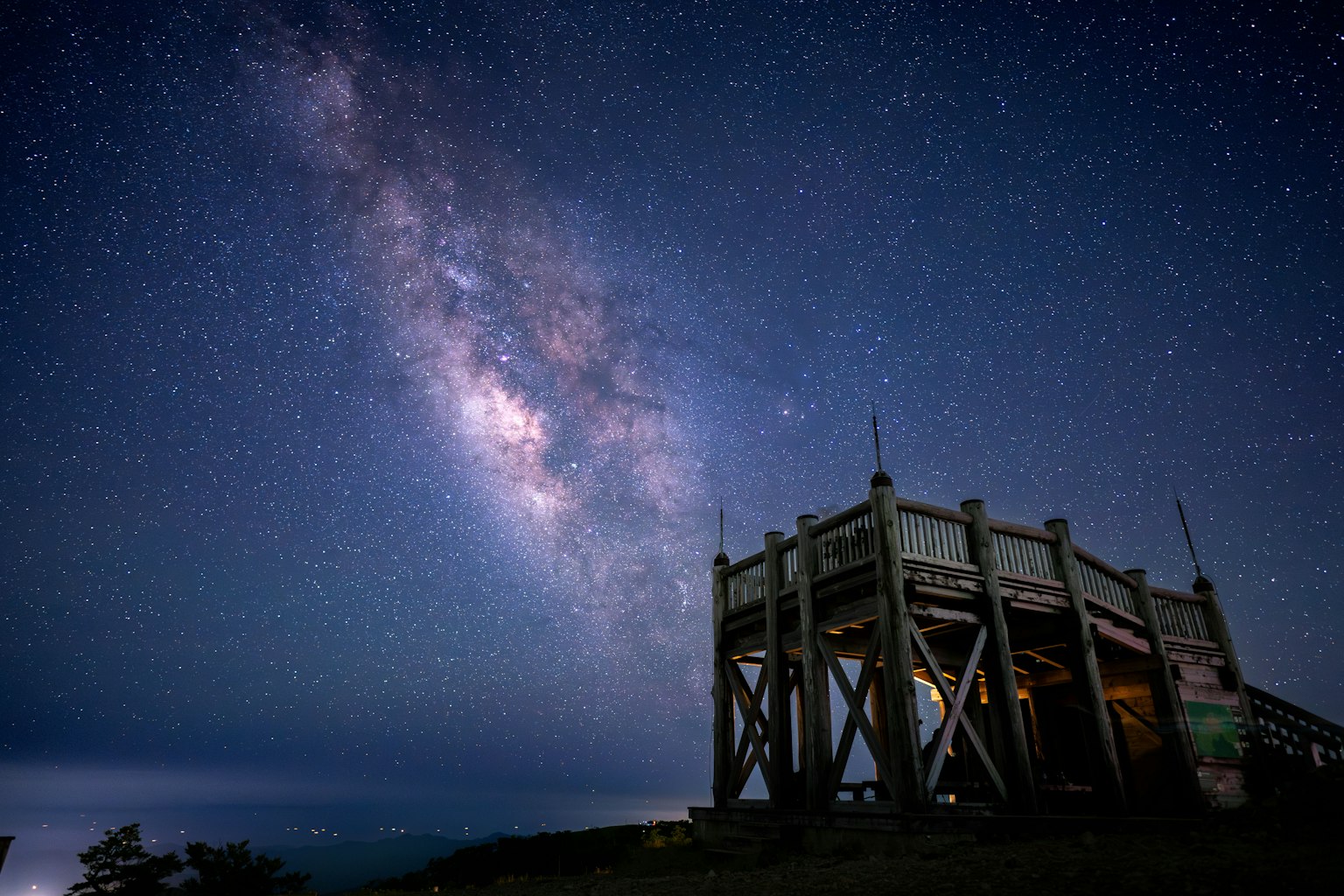 Mirador de madera bajo un cielo estrellado con una vista impresionante de la Vía Láctea