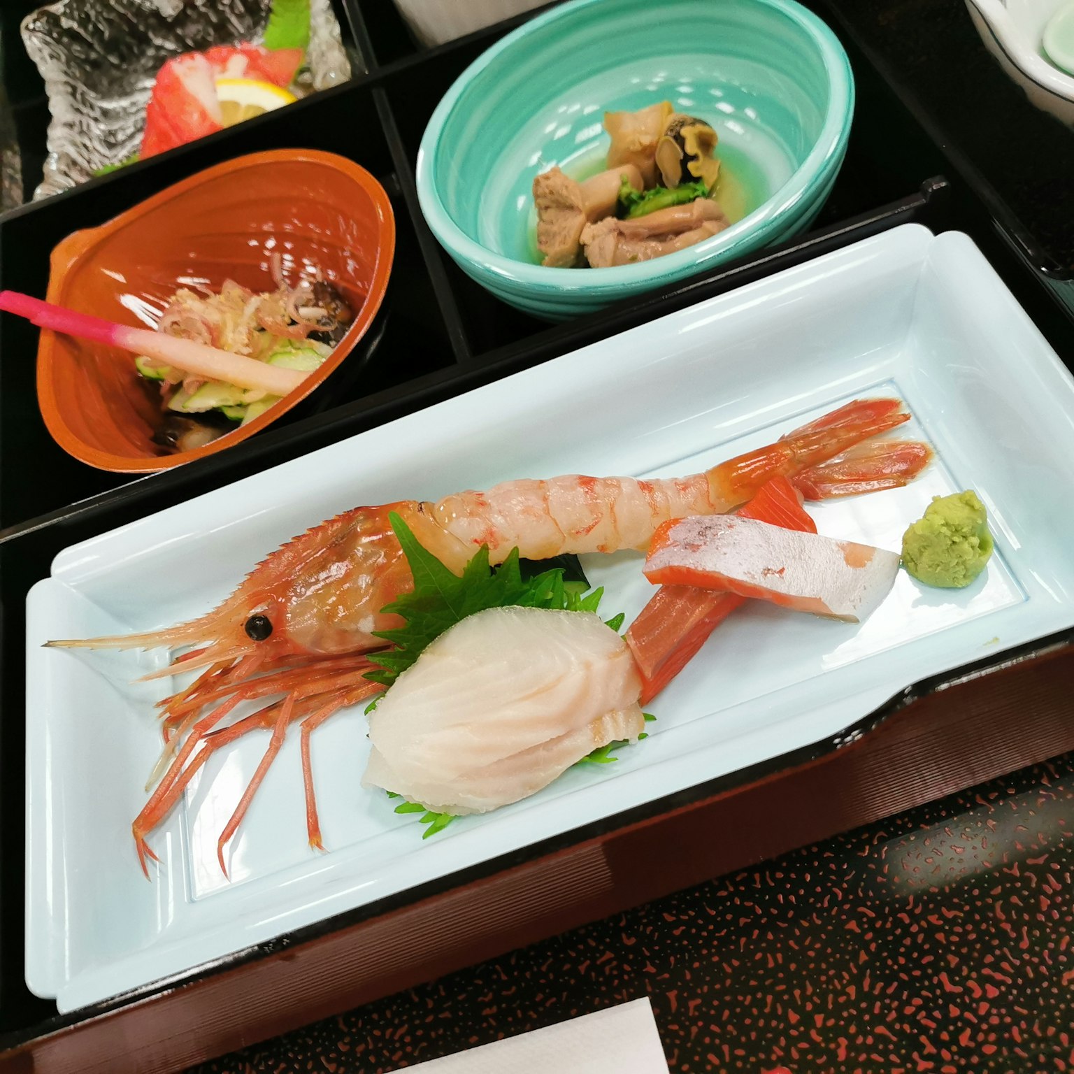 A plate featuring fresh shrimp and sashimi with wasabi and garnishes