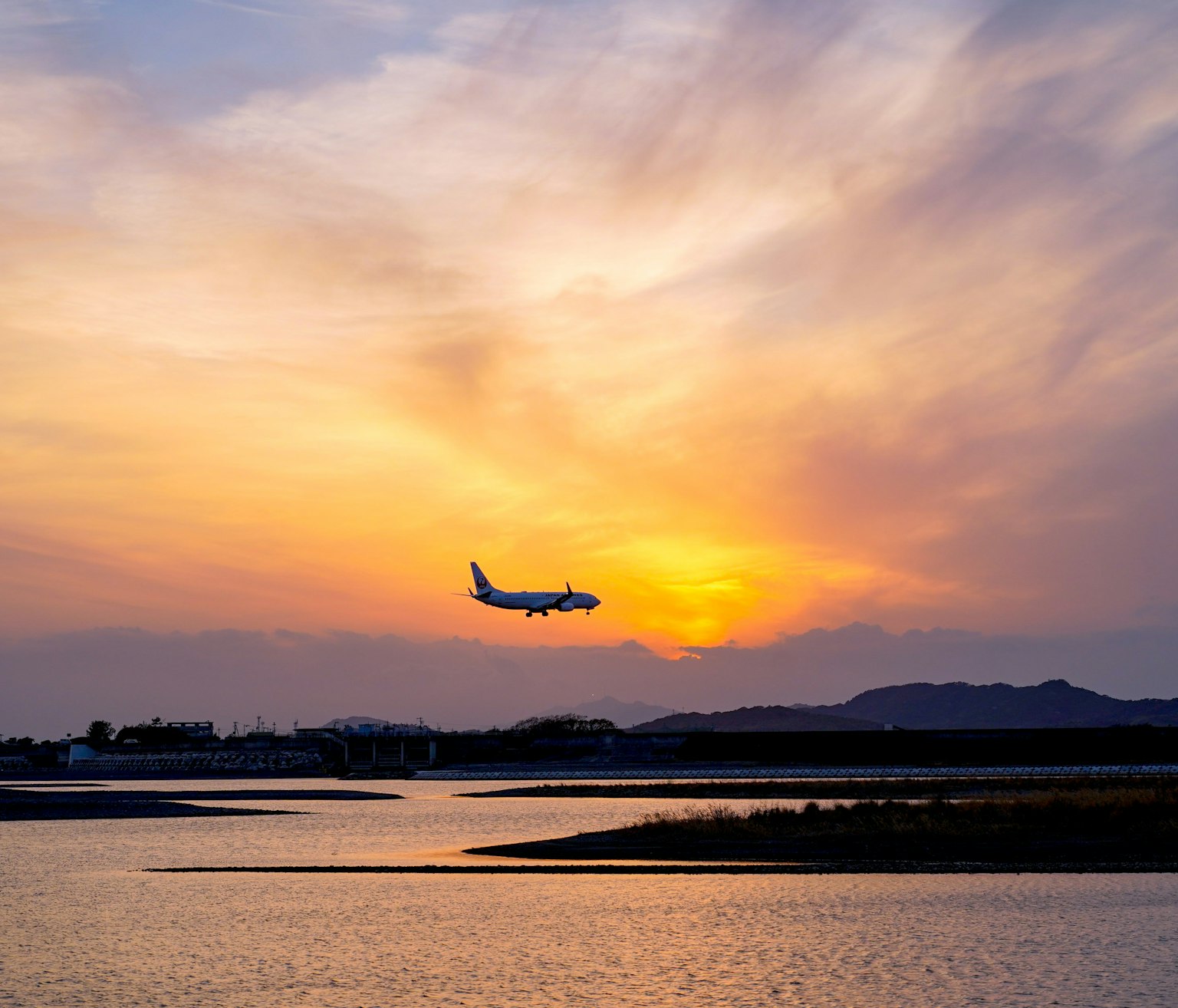 Un aereo che vola sotto il tramonto con un cielo arancione riflesso nell'acqua