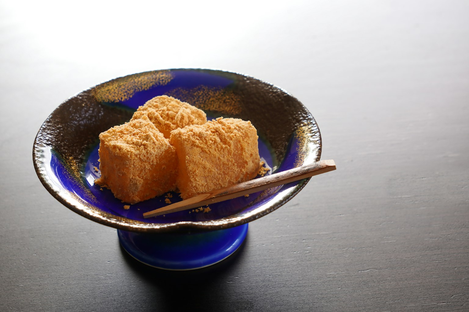 Kubus tahu goreng di piring biru dengan sumpit
