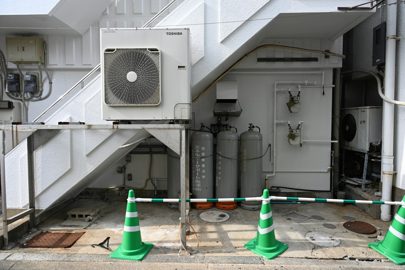 Vue d'une unité de climatisation et de cylindres gris sous un escalier cônes verts et mur blanc