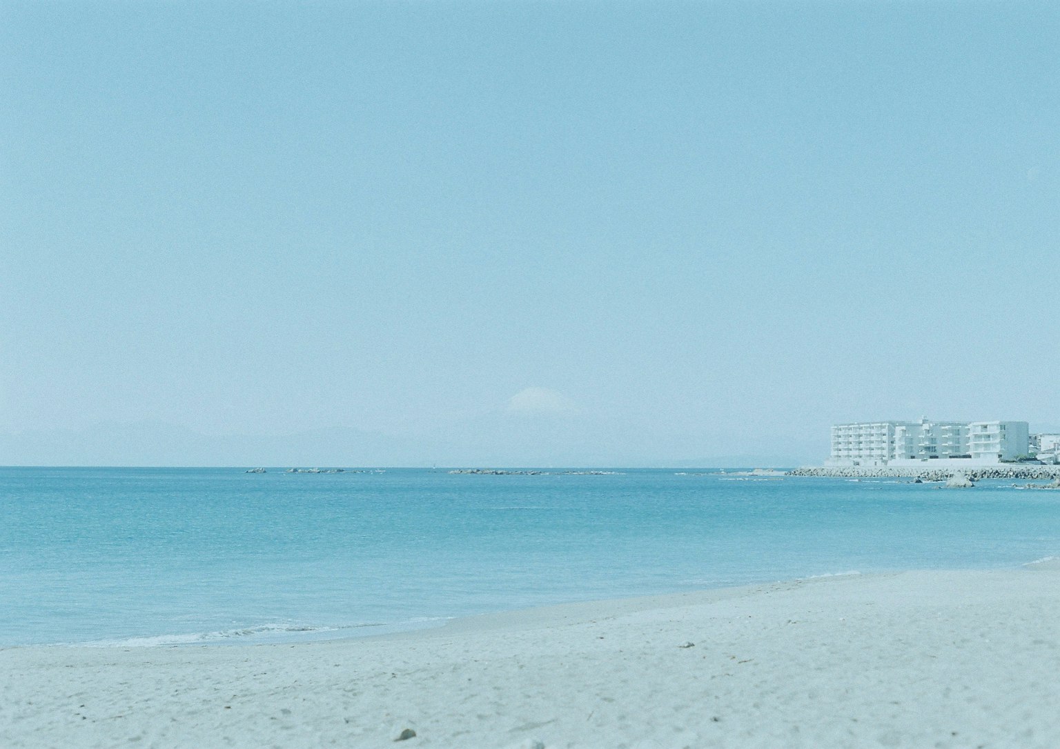 Paesaggio di spiaggia sabbiosa e oceano blu con edifici in lontananza