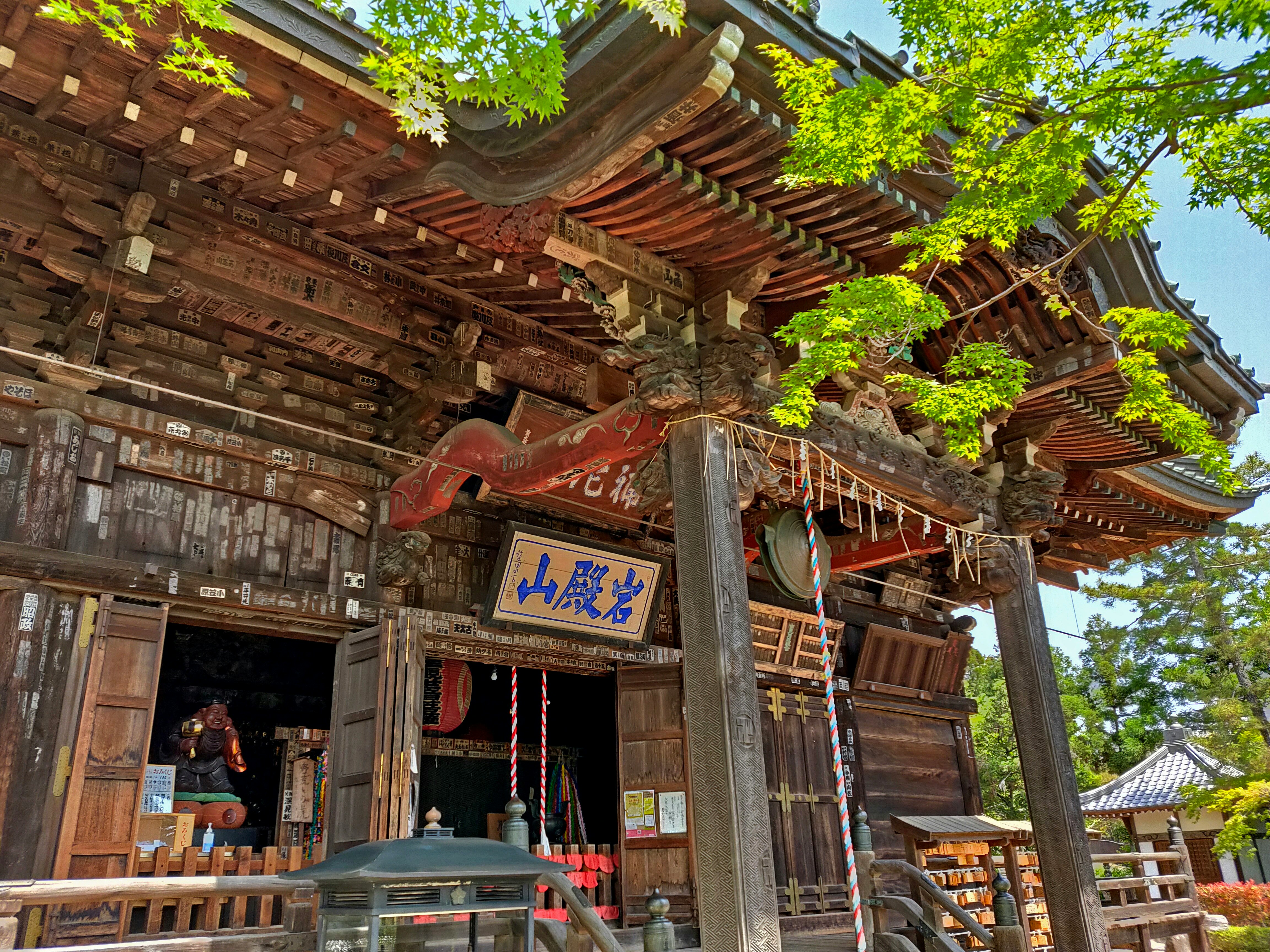 藍天下的木質寺廟牌樓與裝飾飛簷，綠葉繁茂