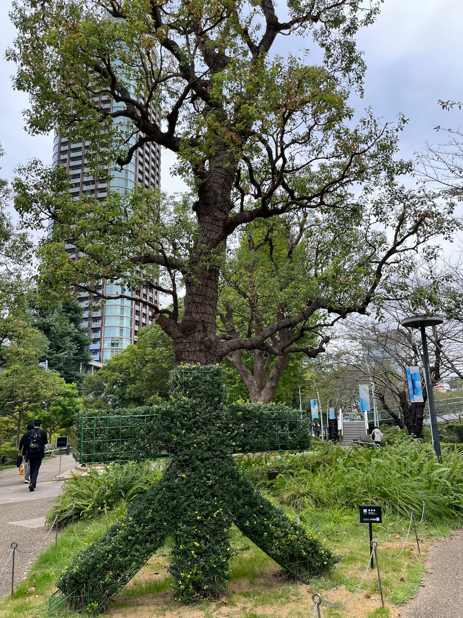 Landschaft mit einem großen Baum und einer grünen Skulptur in einem Park