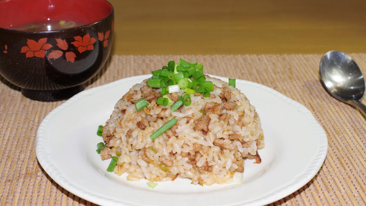 Plato de arroz frito decorado con cebollitas verdes junto a un tazón de sopa