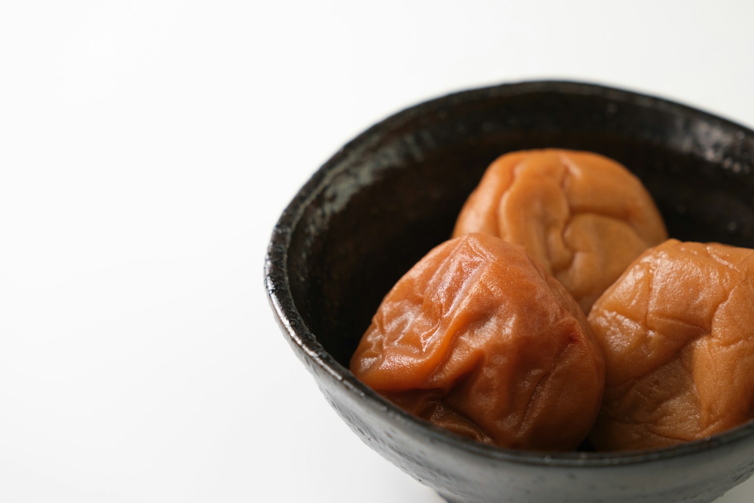 黑碗中的腌制梅子的照片