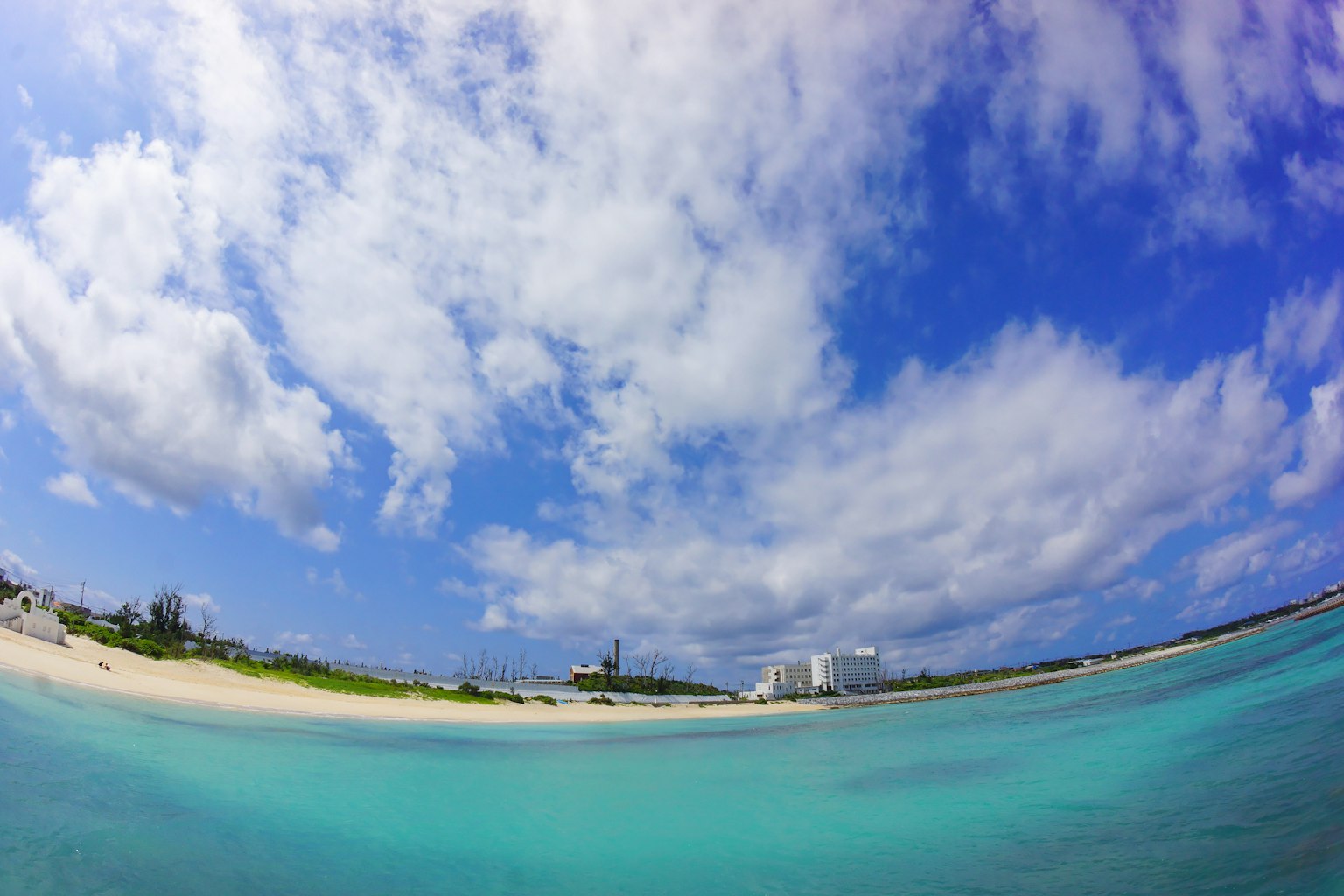 Vista panoramica del mare blu e della spiaggia di sabbia bianca sotto un cielo blu con un faro in lontananza