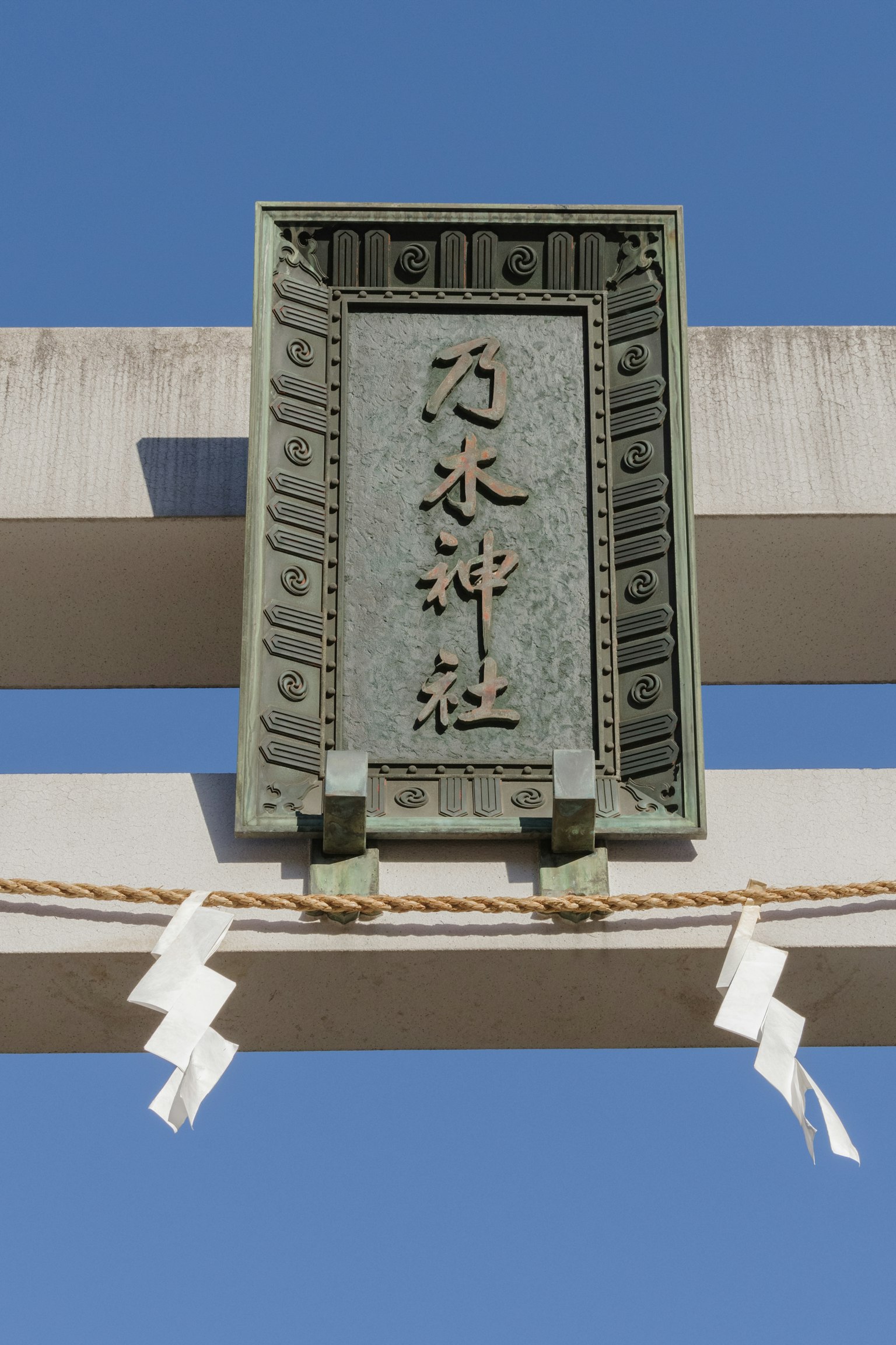 Cartel de bronce montado en un torii de santuario bajo un cielo azul