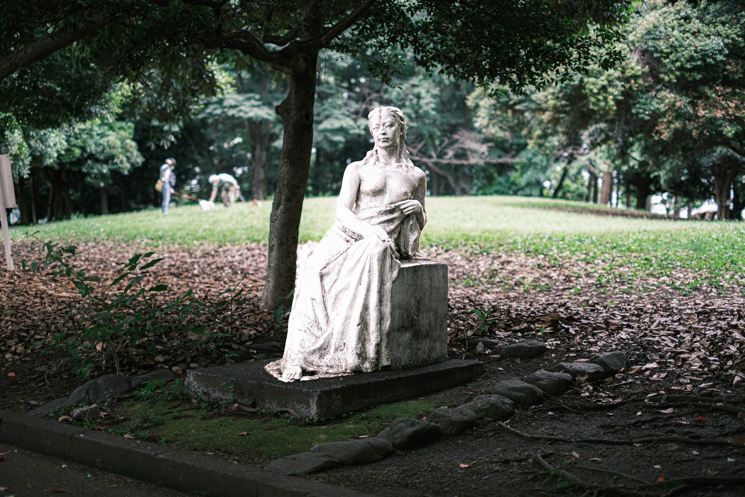 Statua bianca seduta in un parco circondata da alberi verdi
