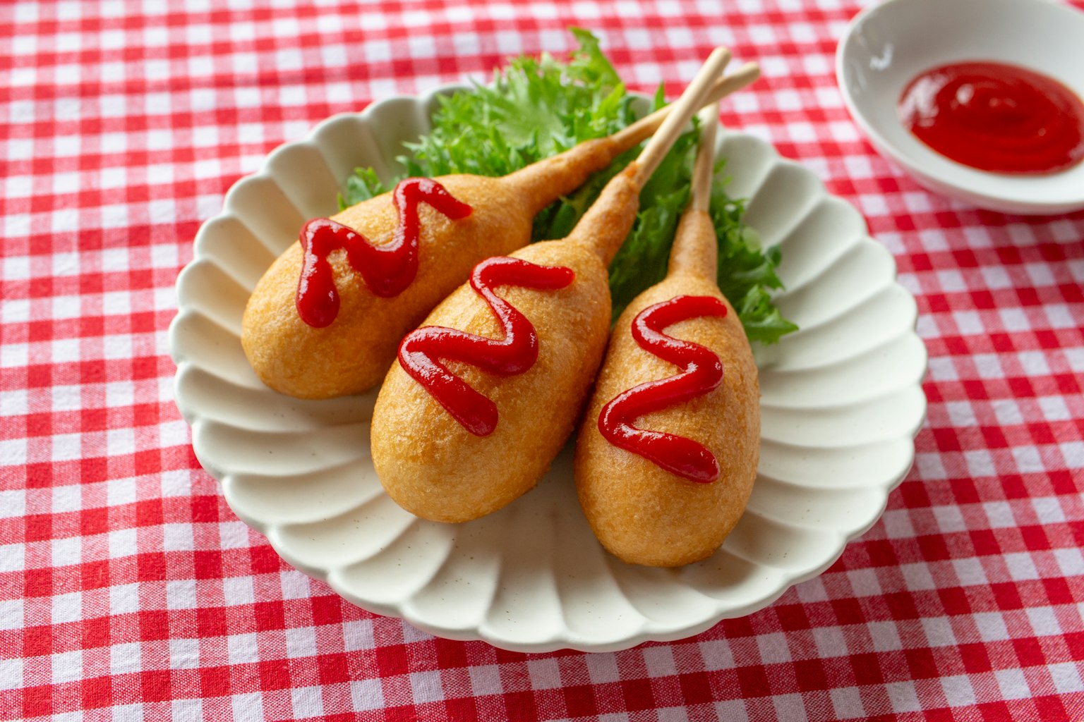 Tre corn dog disposti su un piatto bianco con ketchup sopra