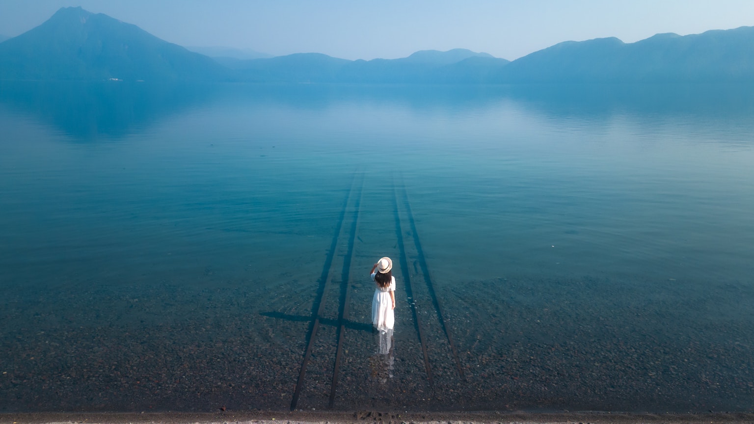 Una mujer en un vestido blanco de pie en un lago azul con sombras